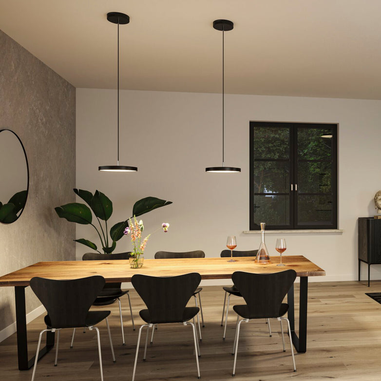 A modern dining room showcases a wooden table, black chairs, and sleek pendant lights equipped with advanced LED technology. The Paulmann Hildor 30W LED Ceiling Light in Black Matt/Chrome, featuring a 3-step dimming function and offering 2100 lumens, beautifully complements the window view.