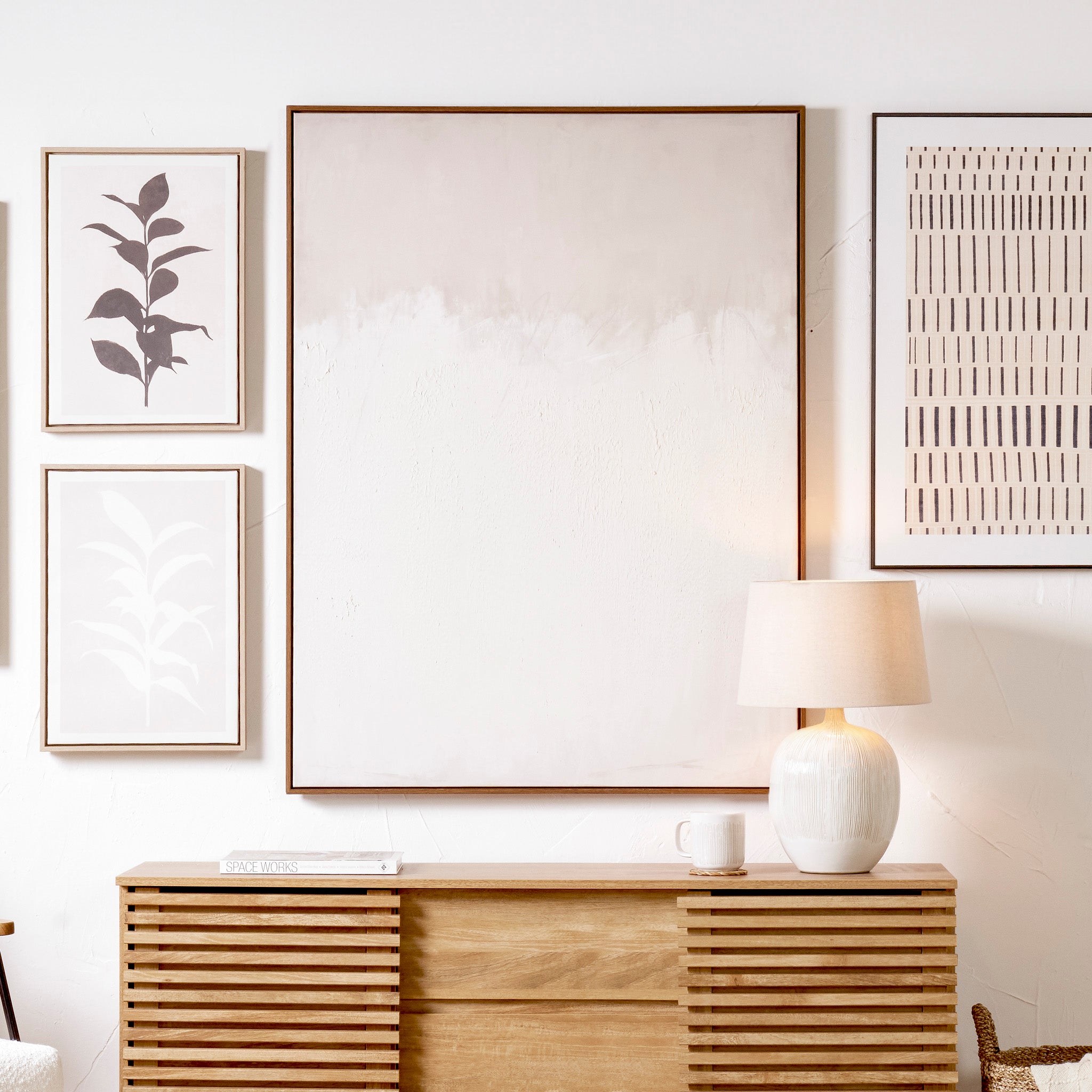 The "Natural and White Abstract Canvas with Natural Frame Large," displayed alongside a wooden console adorned with a lamp and mug, seamlessly complements interior styles with its neutral tones and minimalist design.