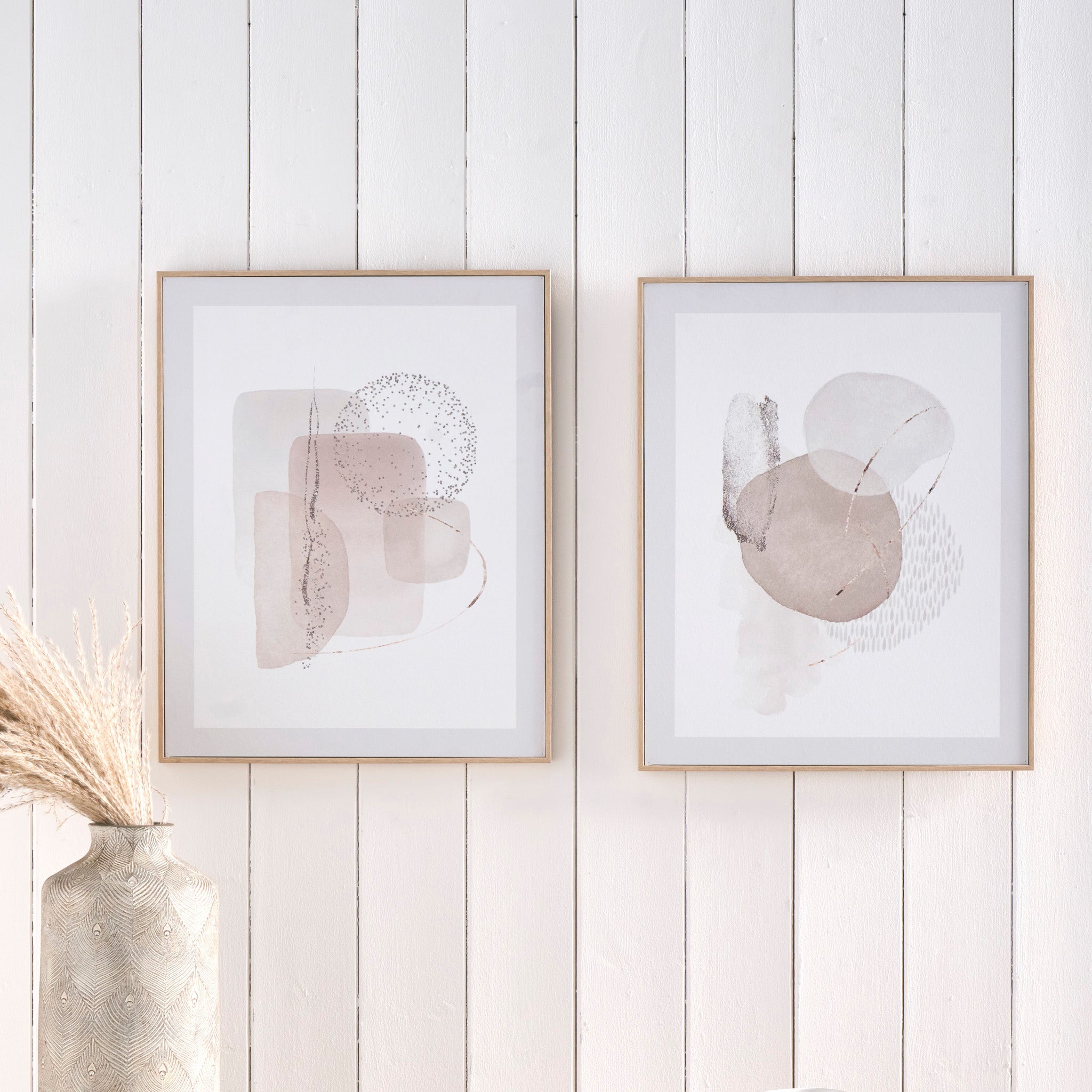 Two pieces of the "Natural Abstract Canvases with Natural Frame" in neutral tones adorn a white wooden wall, accompanied by a vase with dried plants.