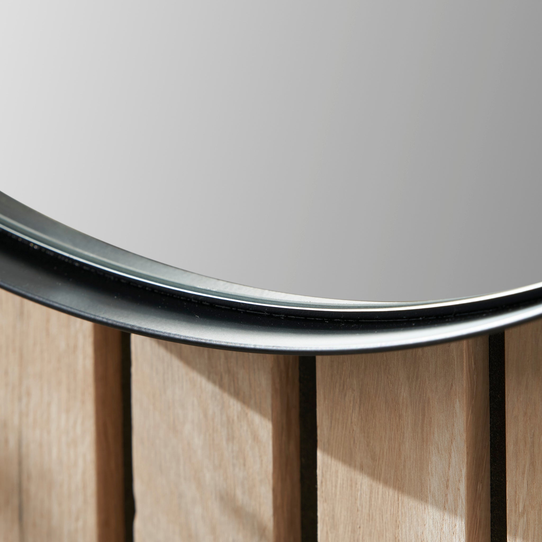 Close-up of a round wall mirror featuring a slim metal frame in brushed silver, set against a wooden panel background.