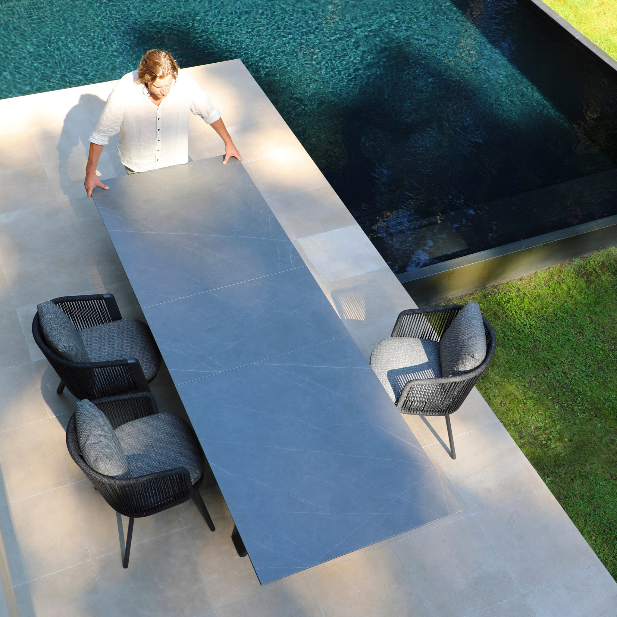 Placing a long Dekota 8 Seat Rope Extending Dining Set in Charcoal beside the pool creates the perfect outdoor space with both style and functionality, making it an ideal gathering spot.