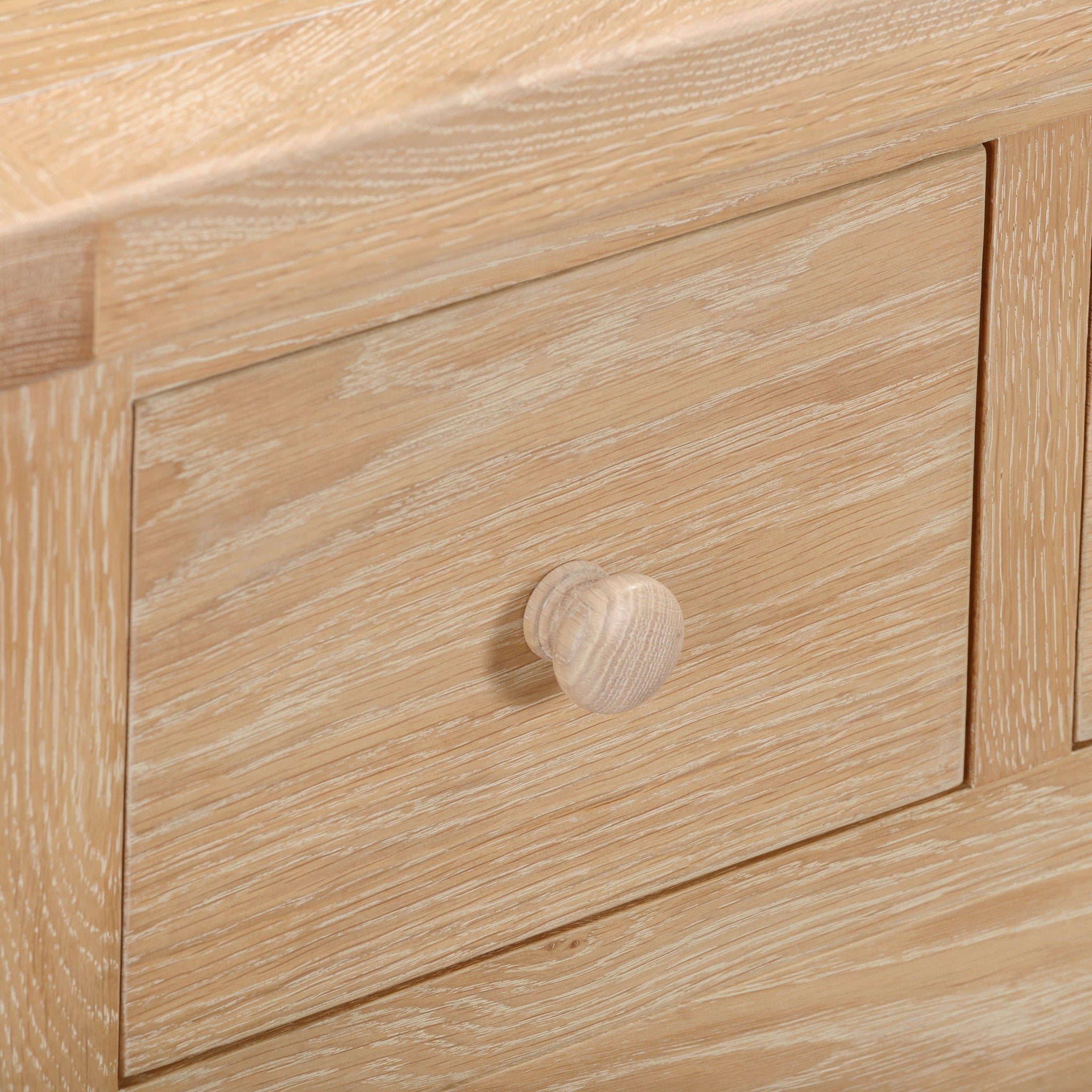 Close-up of a wooden drawer from the Burford 3 Over 4 Chest of Drawers in Natural Oak, showcasing a round wooden knob with a light oak finish and natural wood grain pattern for a rustic aesthetic.