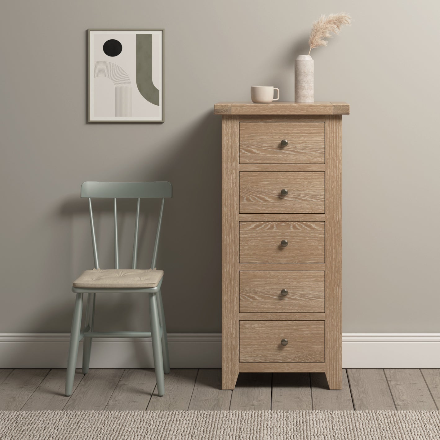 The Burford 5 Chest of Drawers in Natural Oak stands tall beside a light green chair beneath a framed abstract art piece. This wooden dresser offers ample storage solutions with its five spacious drawers.