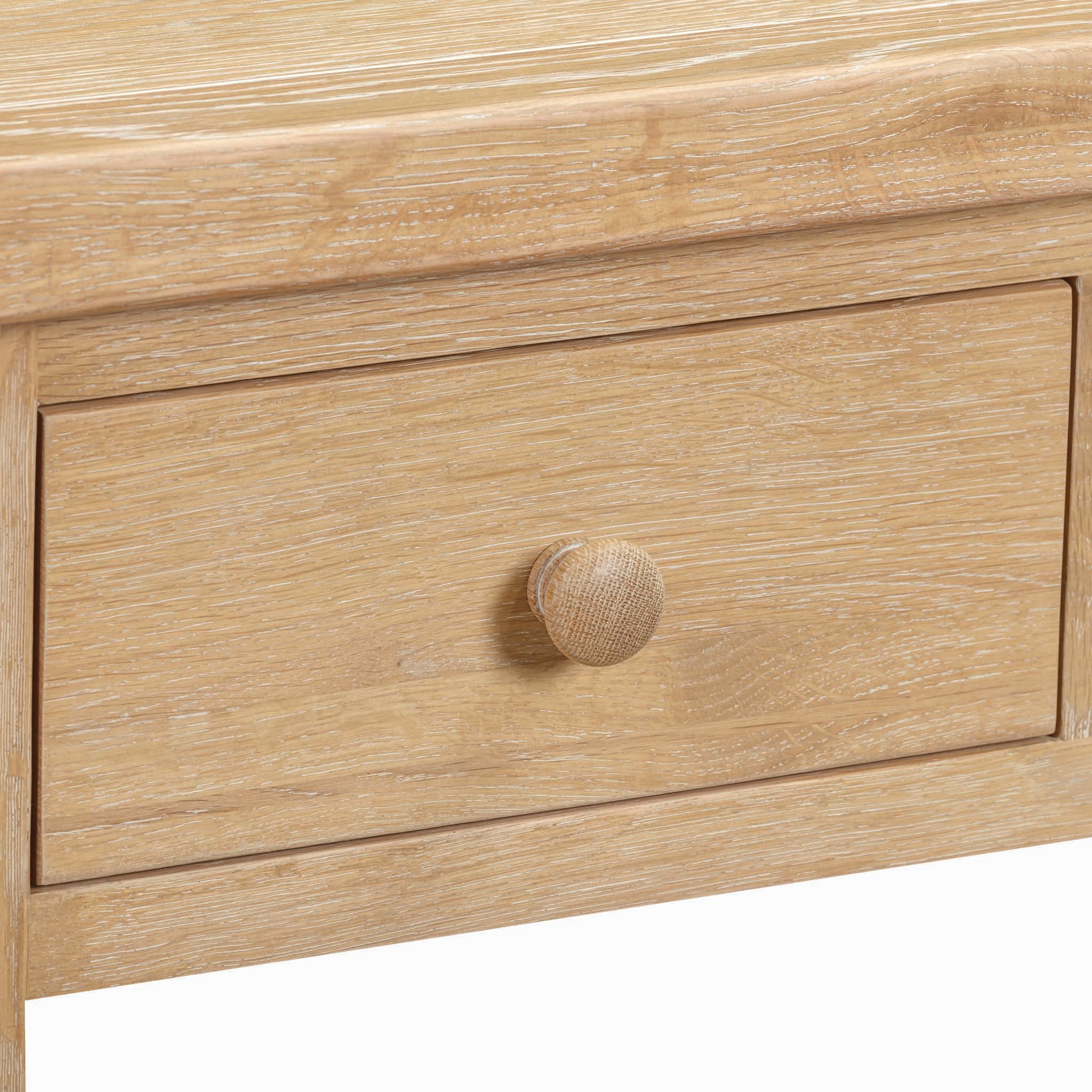 A close-up image of the Burford 2 Drawers Console Table in Natural Oak, featuring a wooden drawer with a round knob on a textured surface, showcasing the fine craftsmanship of these storage drawers.