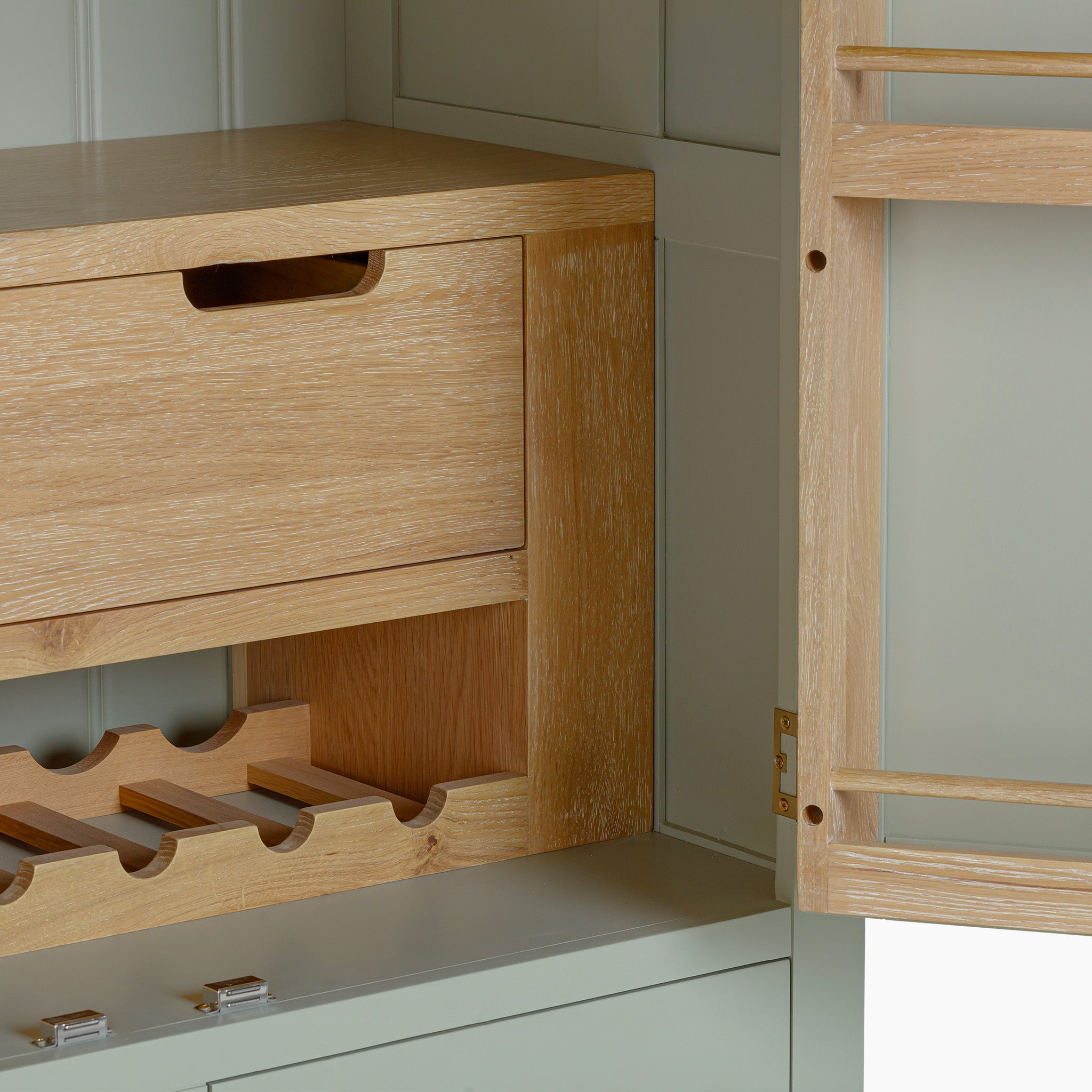 The Burford Double Larder Unit in Sage Green features an open cabinet complete with a natural oak wooden drawer and wine rack, all highlighted by its sage green interior.