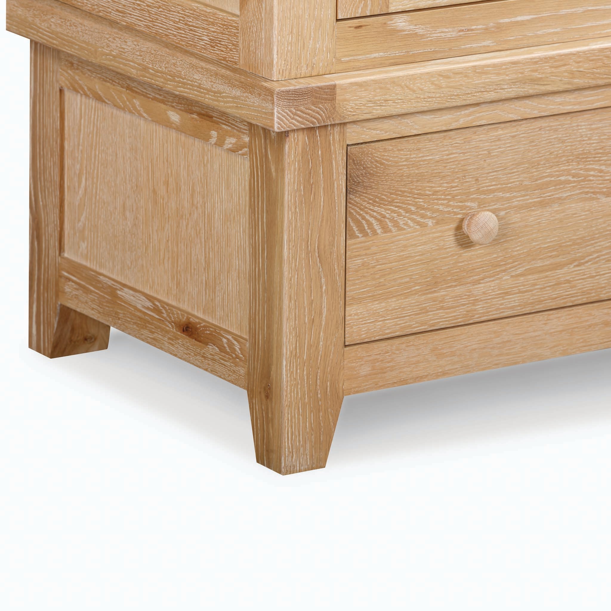 Close-up view of a light wood drawer and leg of the Burford Double Wardrobe with Drawer in Natural Oak, showcasing its visible wood grain and round knob, exemplifying the quality craftsmanship typical of this natural oak furniture piece.