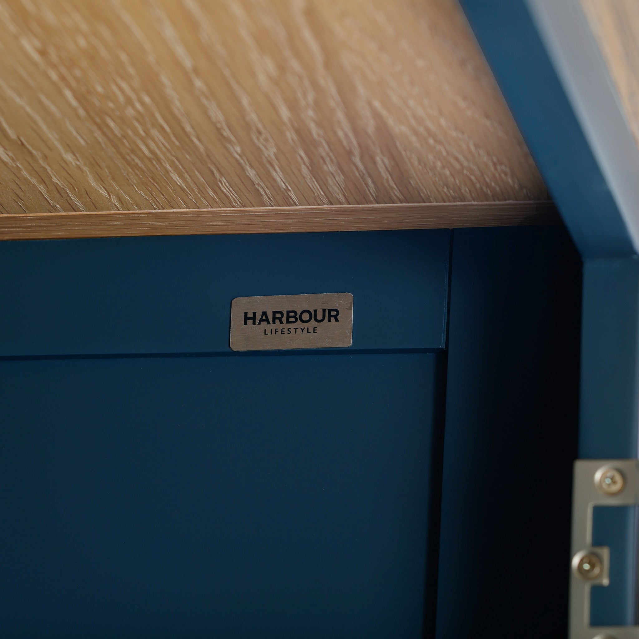 Close-up of a corner of the Burford Display Cabinet in Navy Blue, featuring a "Harbour Lifestyle" label beneath a natural oak surface.