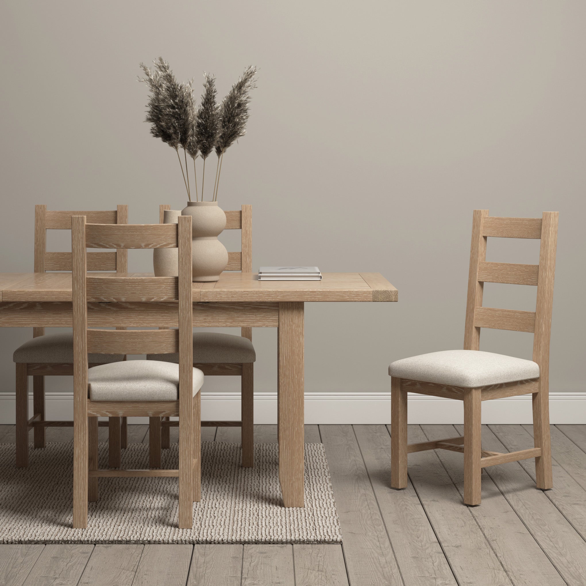 Minimalist dining area with a natural oak wooden table and chairs, beige cushions, dried plants in a vase, and neutral decor. The rustic touch is complemented by the versatile Burford 4-6 Seater Extending Dining Table in Natural Oak.