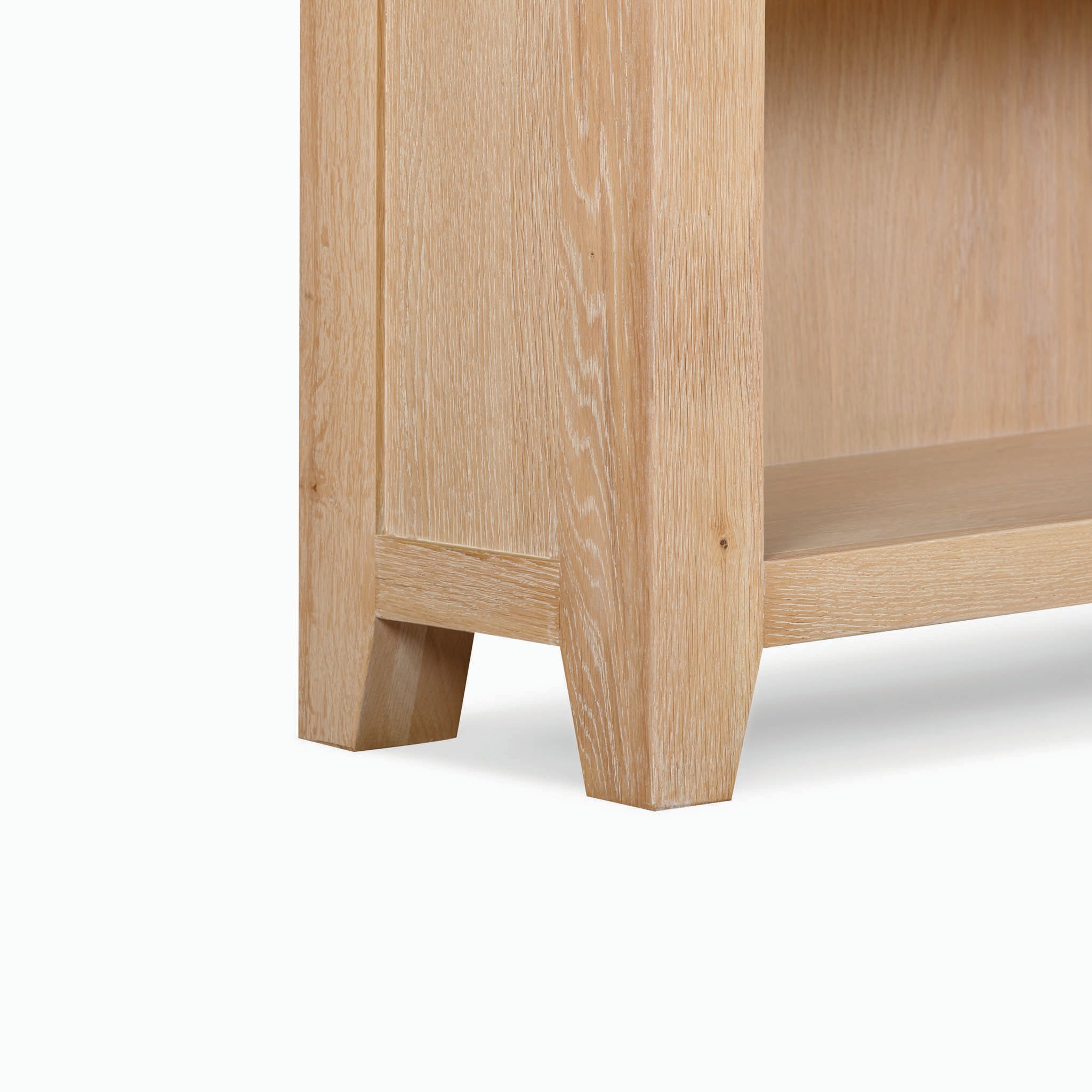 Close-up of the lower corner of the Burford Large Bookcase in Natural Oak, showcasing its light-colored wood grain, sturdy legs, and touch of contemporary elegance.