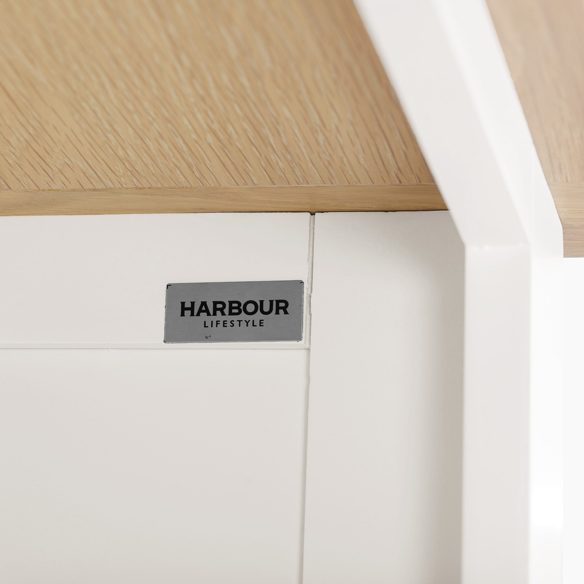 Close-up of the Burford Large Bookcase in Warm White showcasing a white frame with a natural oak top and the "Harbour Lifestyle" label attached, providing ample shelving space for your needs.