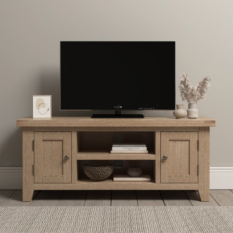 A minimalist TV stand showcasing contemporary elegance holds a flat-screen TV, decor items, books, and a textured basket on a neutral background. The addition of the Burford 120cm Media Unit in natural oak seamlessly elevates the aesthetic.