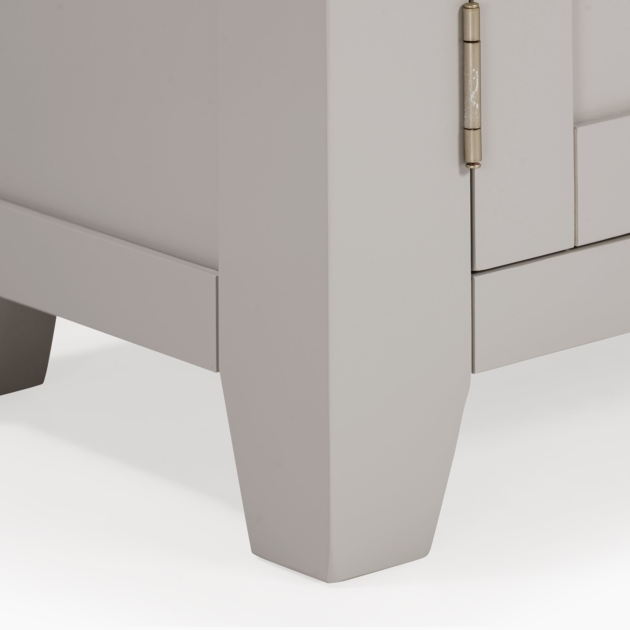 Close-up of the bottom corner of the Burford 120cm Media Unit in Pebble Grey, highlighting its sturdy hinge and angular legs. The subtle contrast with natural oak elements infuses a touch of elegance.