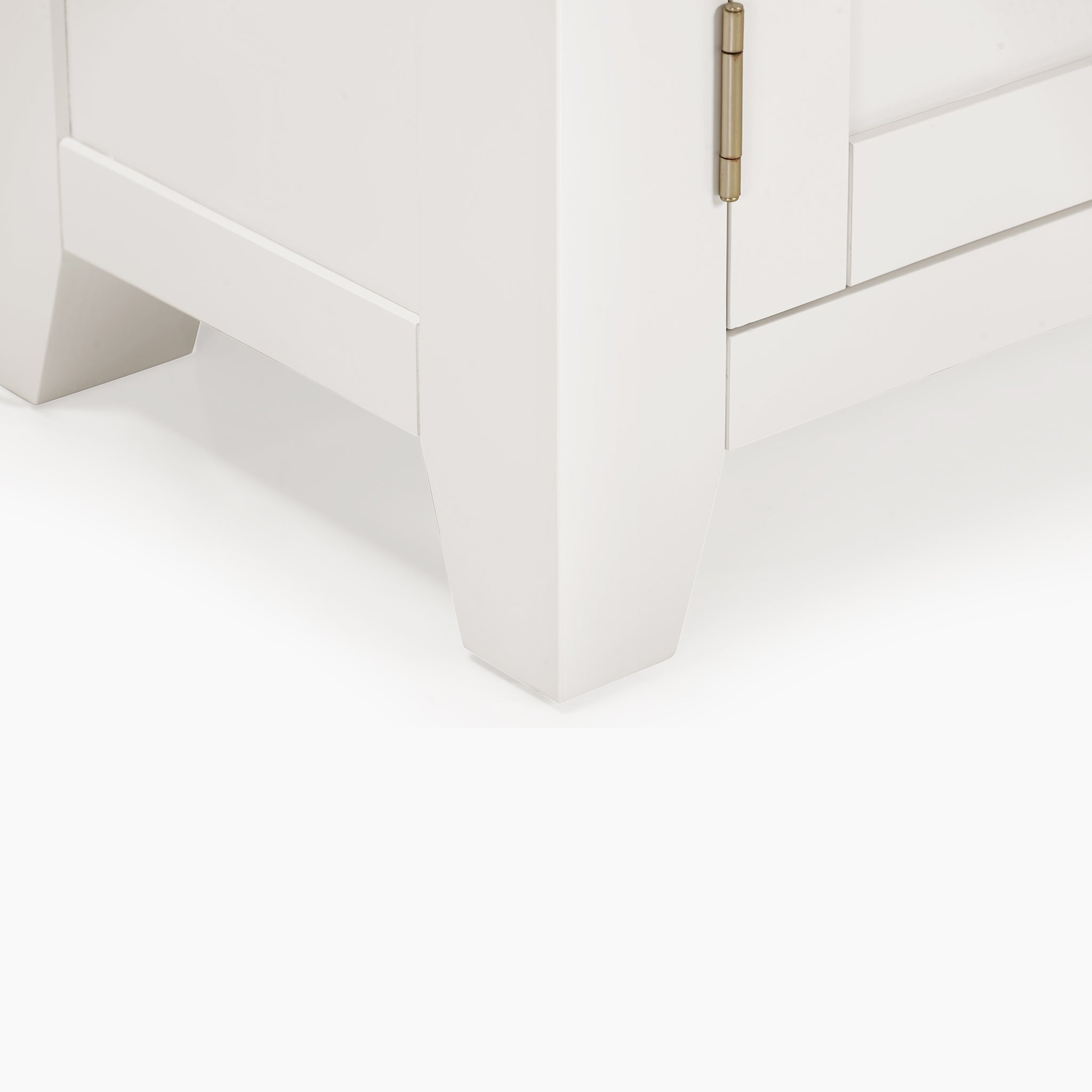 Close-up of the bottom corner of a Burford 120cm Media Unit in Warm White, highlighting its brass hinge and tapered legs that emanate rustic charm beneath a white-washed oak top.