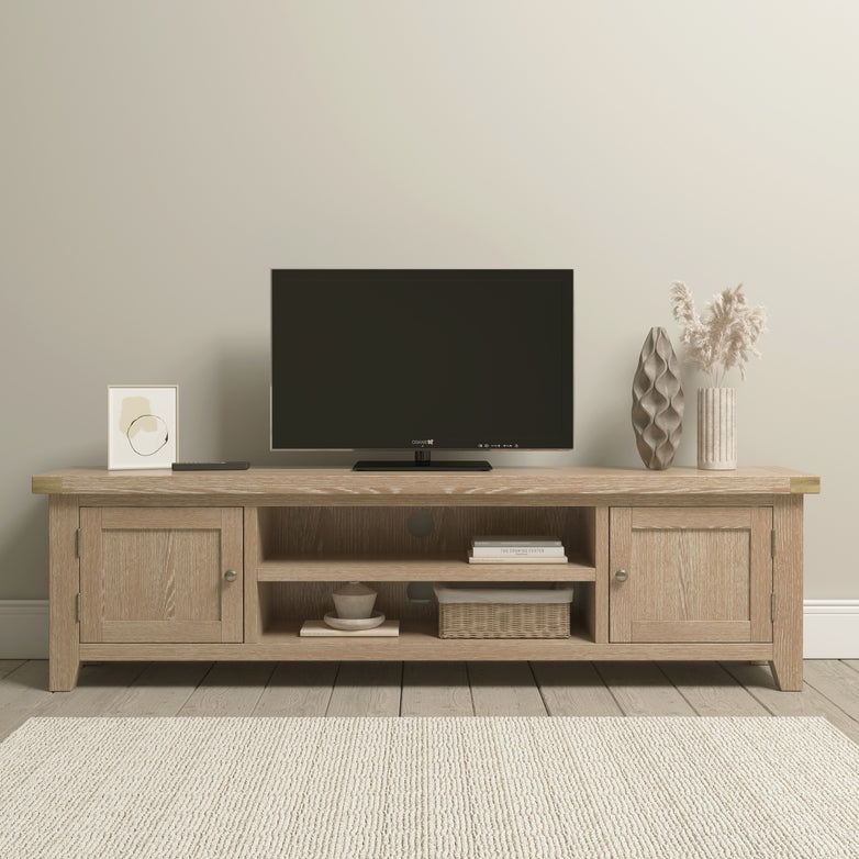 Modern living room featuring the Burford Large 180cm Media Unit in Natural Oak, adorned with a flat-screen TV, decorative vases, framed art, and a soft beige rug. The unit excels in cable management, ensuring a tidy and organized space.