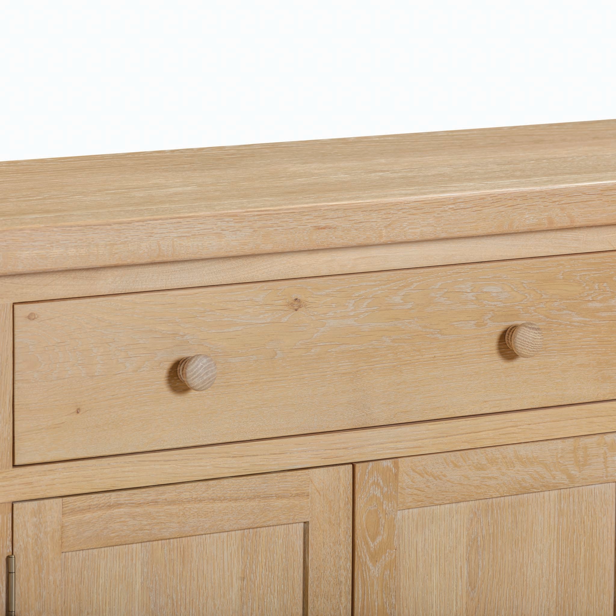 The Burford Large 4 Door 3 Drawers Sideboard in Natural Oak is a stylish piece of storage furniture that features three spacious drawers and four lower cupboards, all adorned with simple round wooden knobs.