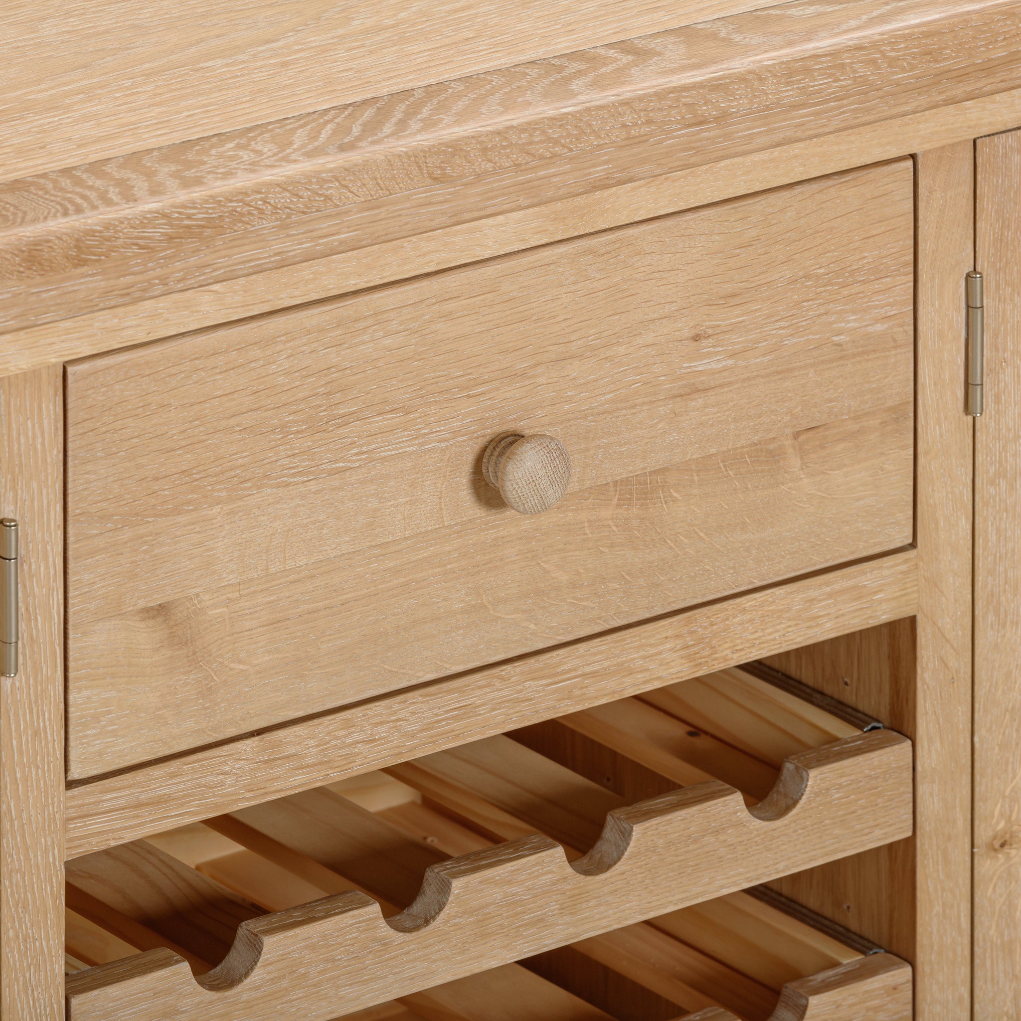 Close-up of the Burford Grand Sideboard with Wine Rack in Natural Oak displaying rustic sophistication, featuring a small drawer, cabinet door, and built-in wine rack holding four bottles.