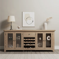 The Burford Grand Sideboard with Wine Rack in Natural Oak, adorned with glass doors, a wine rack, a lamp, framed abstract art, a cup, and an elegant pampas arrangement in a vase on top, radiates rustic sophistication.