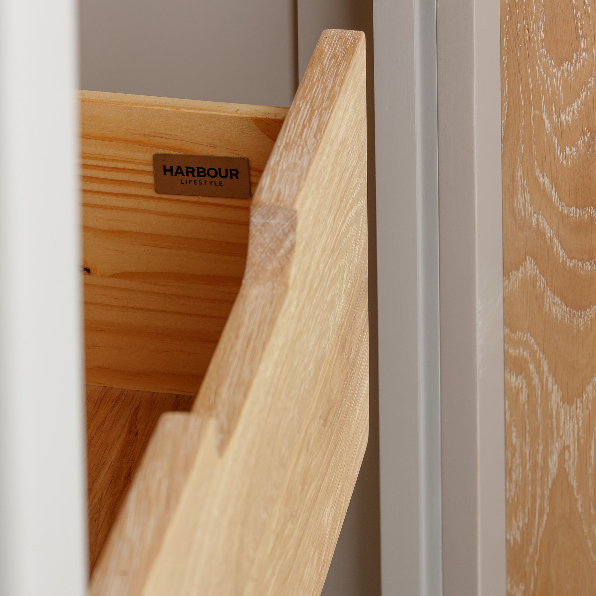 Close-up of a wooden drawer partially open, set in a light-colored cabinet with the label "Burford Single Larder Unit in Pebble Grey" from Harbour Lifestyle, showcasing exquisite natural oak craftsmanship ideal for enhancing your kitchen storage.