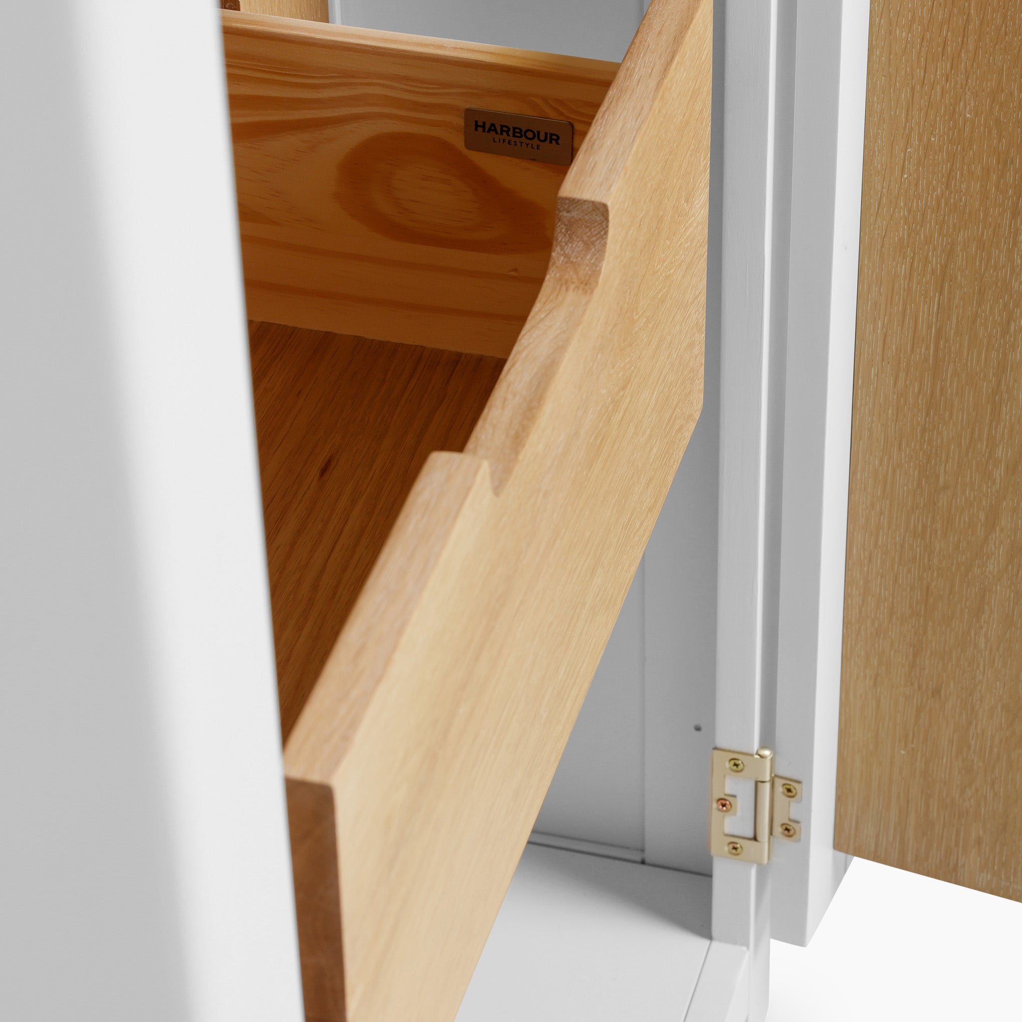 The Burford Single Larder Unit in Warm White showcases an open wooden drawer made from natural oak, skillfully incorporated into a sleek cabinet with a partially open door for stylish kitchen storage.