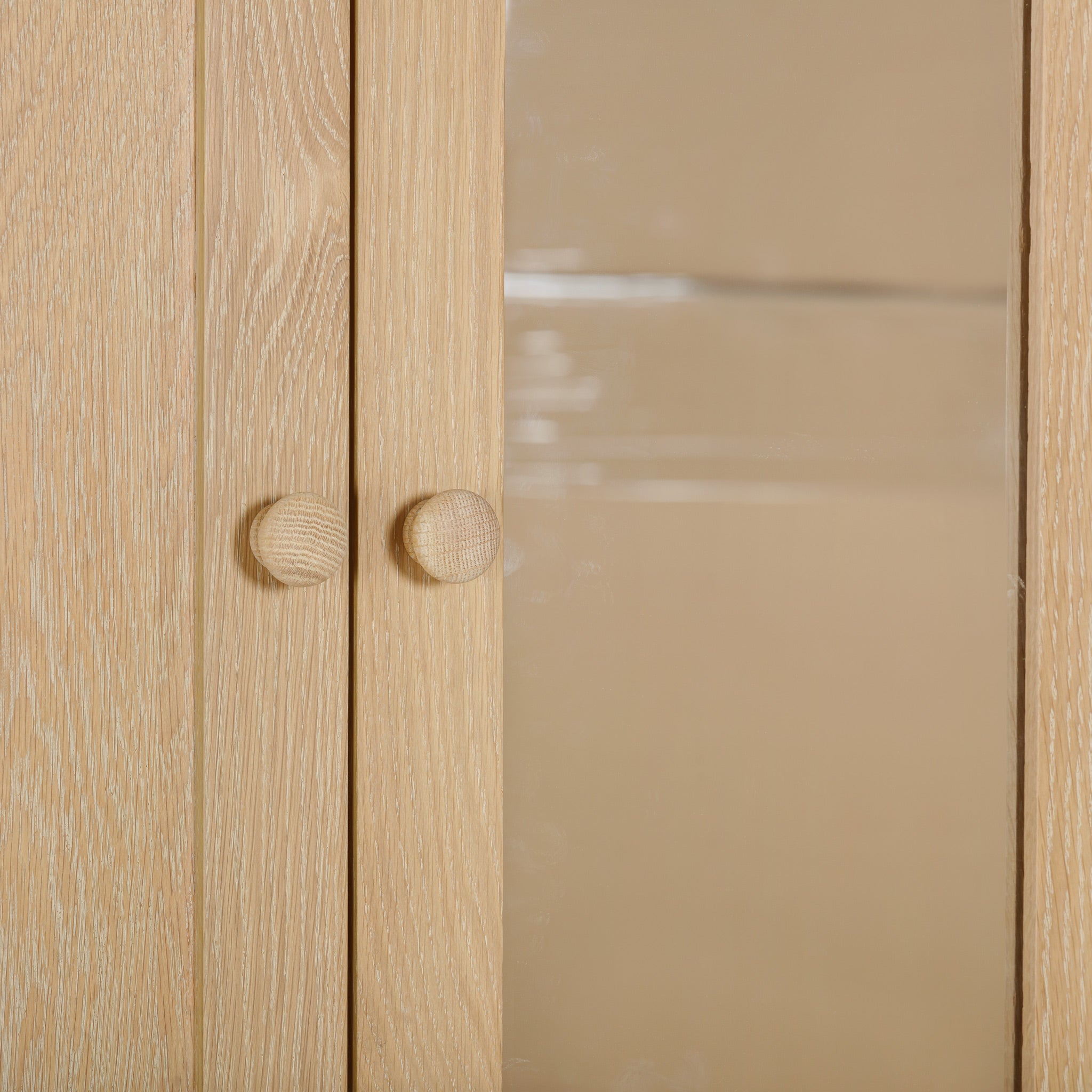 Close-up of a natural oak cabinet door with two round wooden knobs and a glass panel, offering a sneak peek into the Burford Triple Wardrobe with 2 Drawers in Natural Oak—a stylish storage solution.