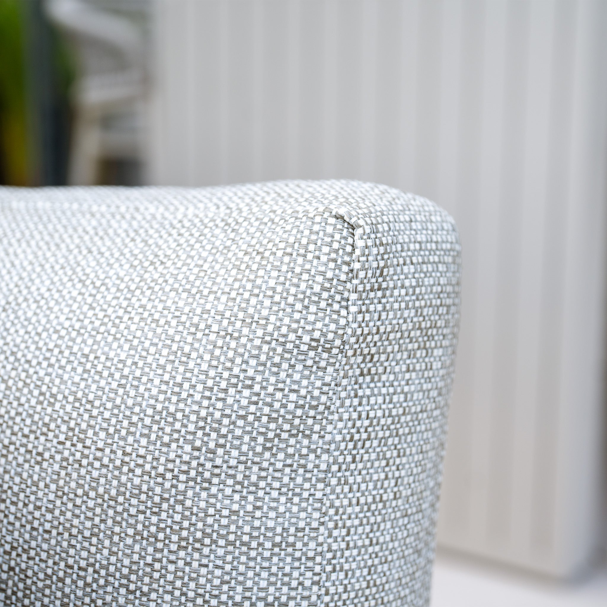 Close-up of the corner of the Bay Corner Group Set with 4 Waist Pillows and Teak Table in Latte, featuring a light gray textured fabric and a powder-coated aluminum frame, set against a blurred background.