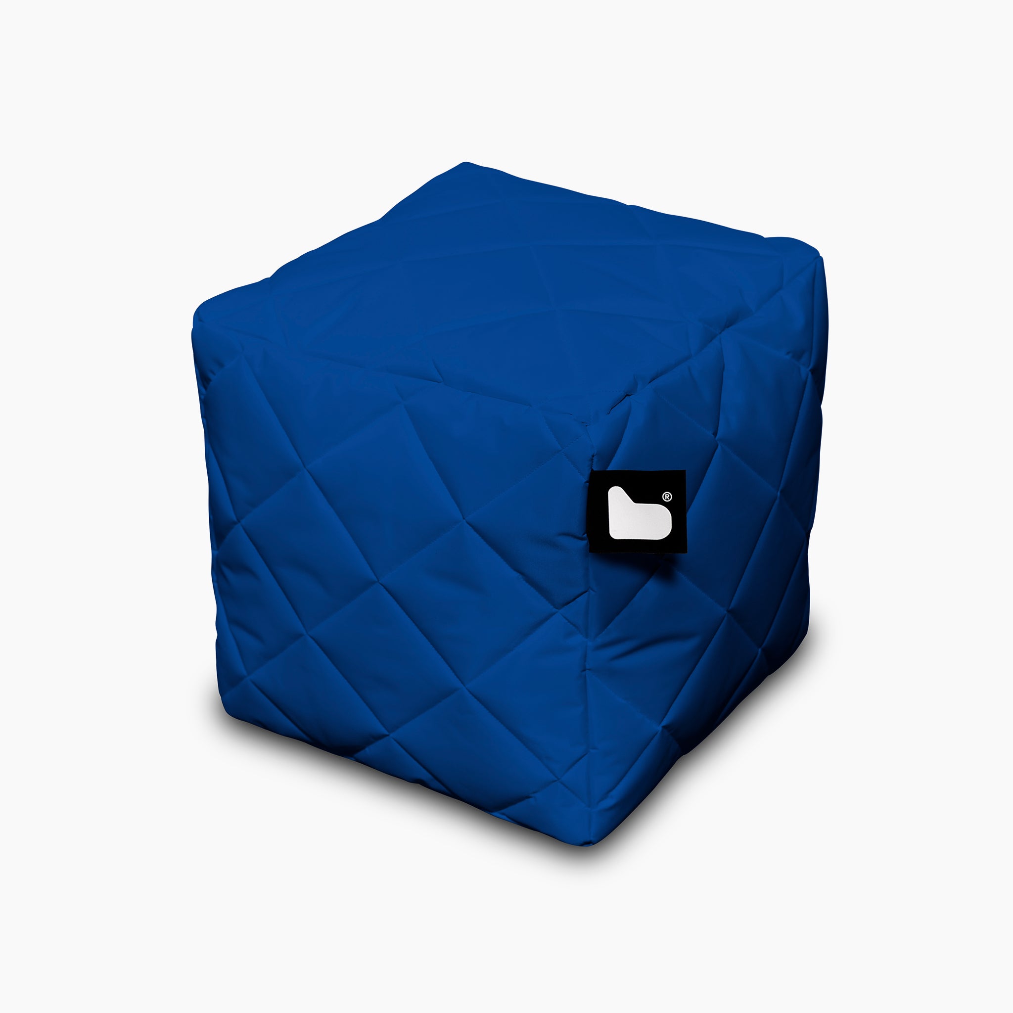 The Outdoor Quilted B-Box in Royal is a blue, cube-shaped pouf with a black tag featuring a white logo on a white background, perfect for extreme lounging.