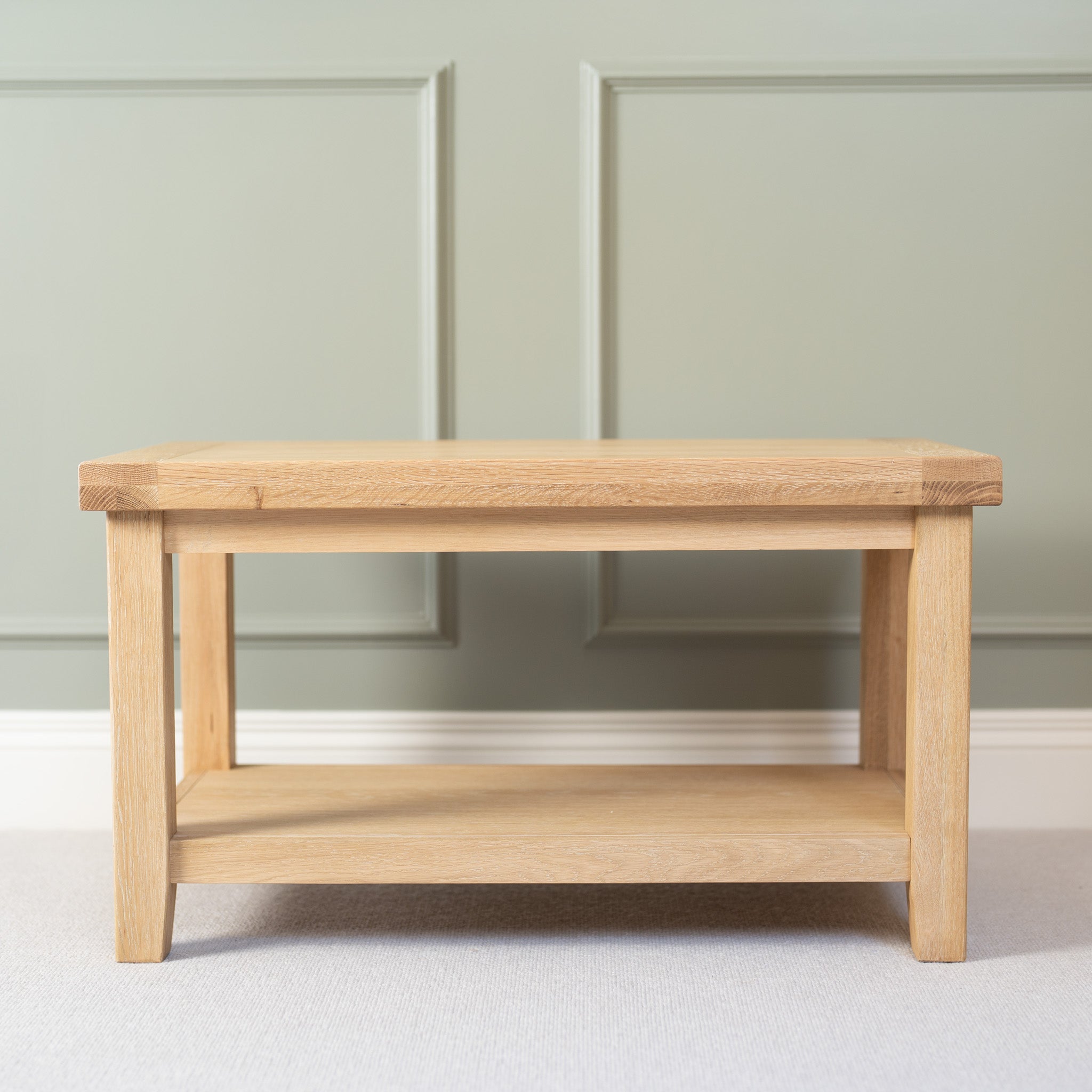 Burford Large Coffee Table with Shelf in Natural Oak set against a light green paneled wall.