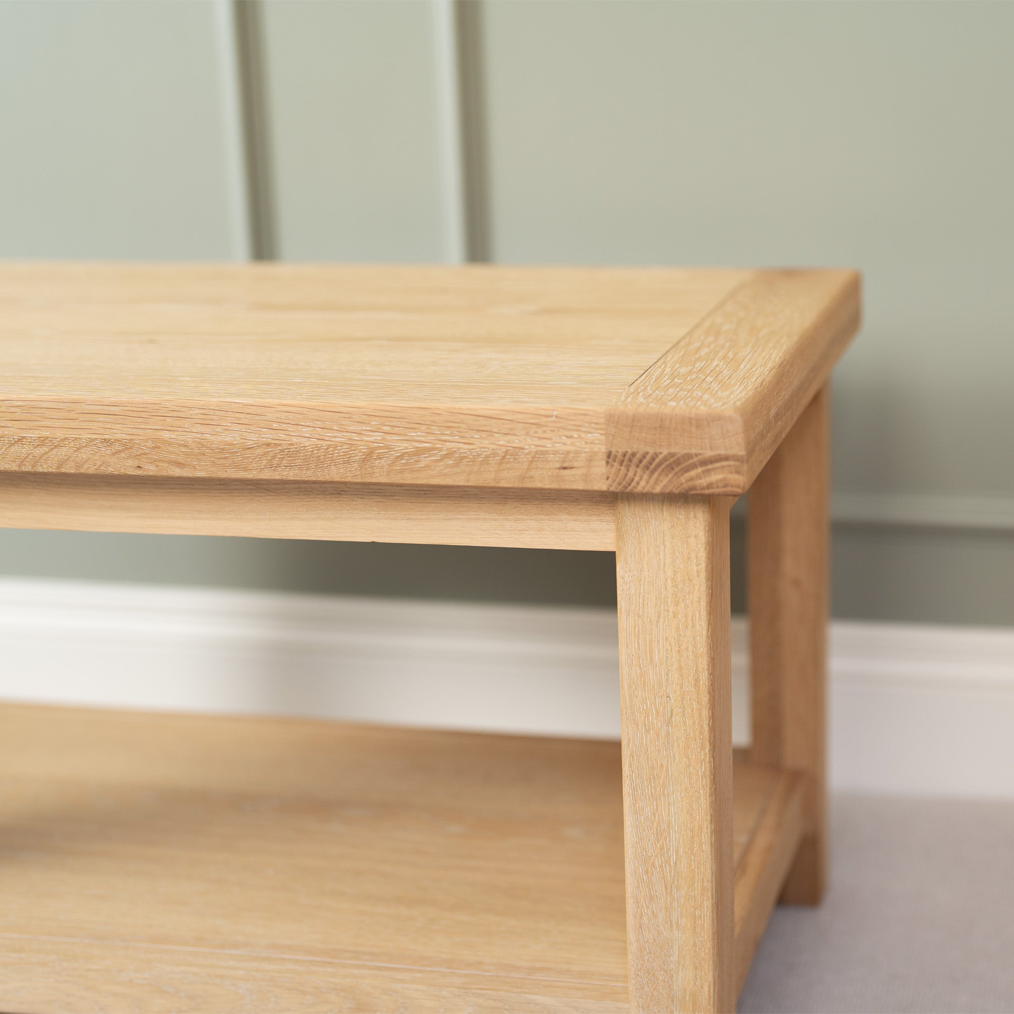 The Burford Large Coffee Table with Shelf in Natural Oak features a light wooden construction and subtle whitewash finish, looking elegant against a muted green wall.