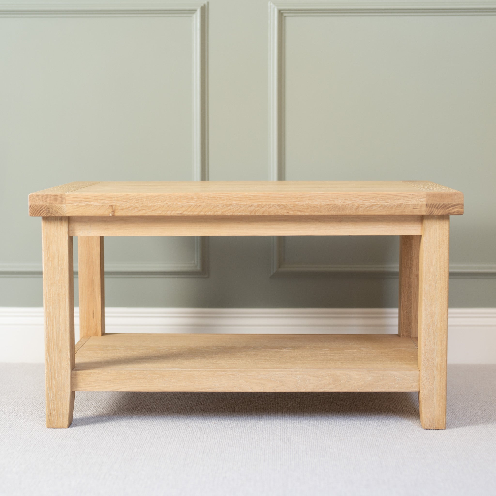 The Burford Large Coffee Table with Shelf in Natural Oak stands against a muted green paneled wall.