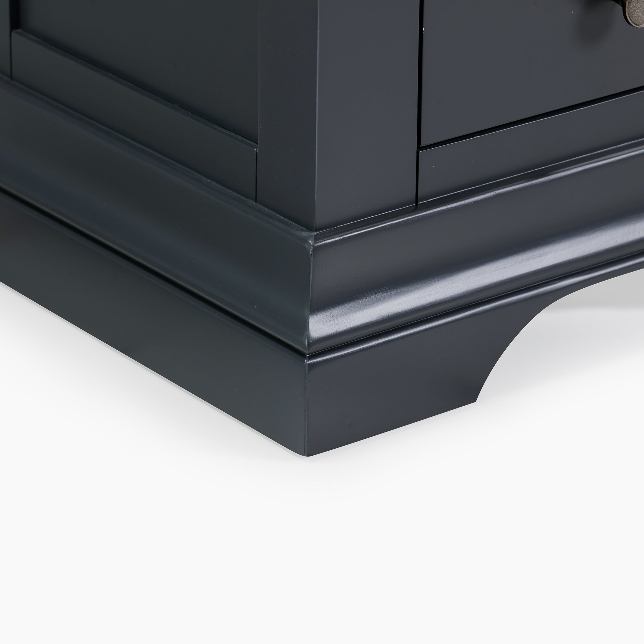 A close-up of the lower corner of a dusky black cabinet highlights a simple decorative base that mirrors the elegance of the Chalbury 3 Drawer Bedside Table in Dusky Black.