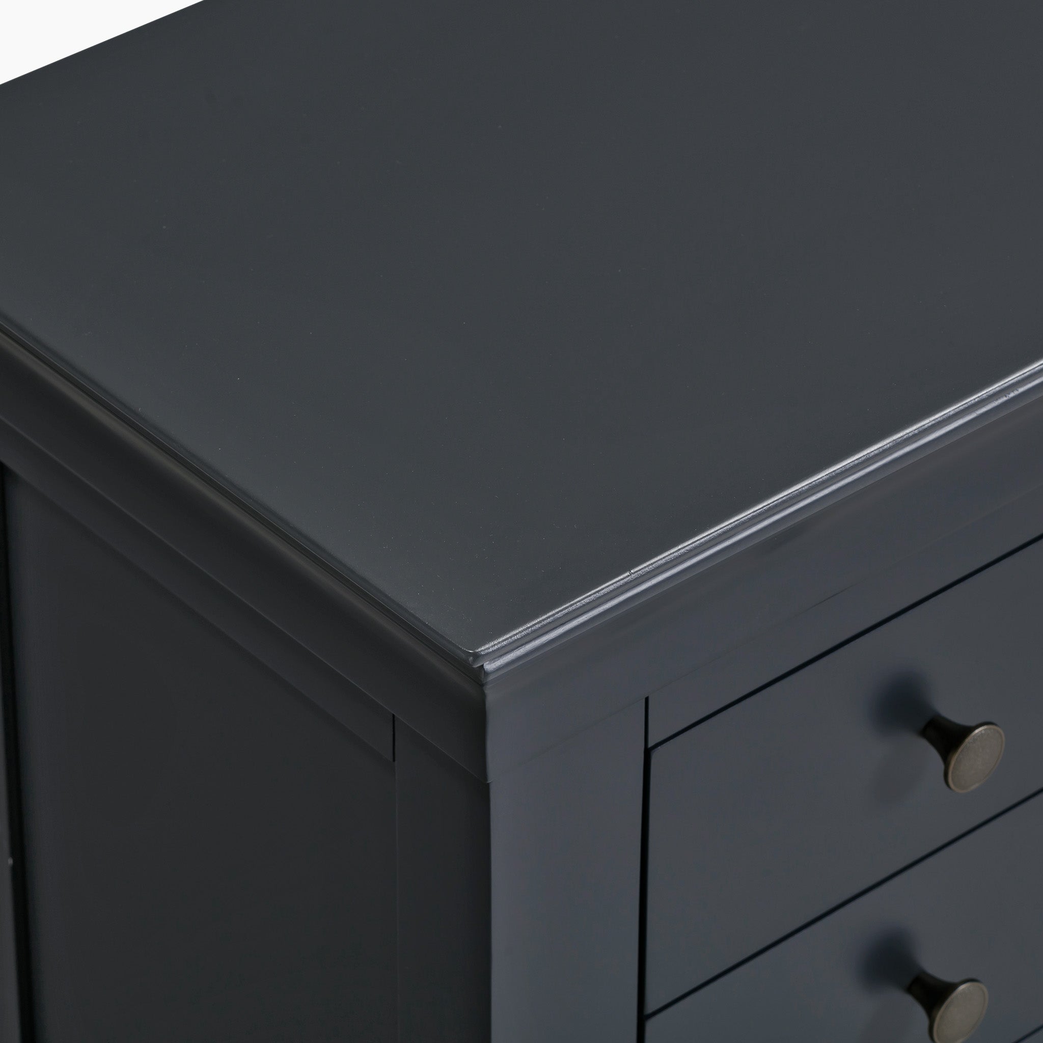 A close-up of the corner of a Chalbury 3 Drawer Bedside Table in dusky black, featuring round metal knobs and crafted from solid oak.