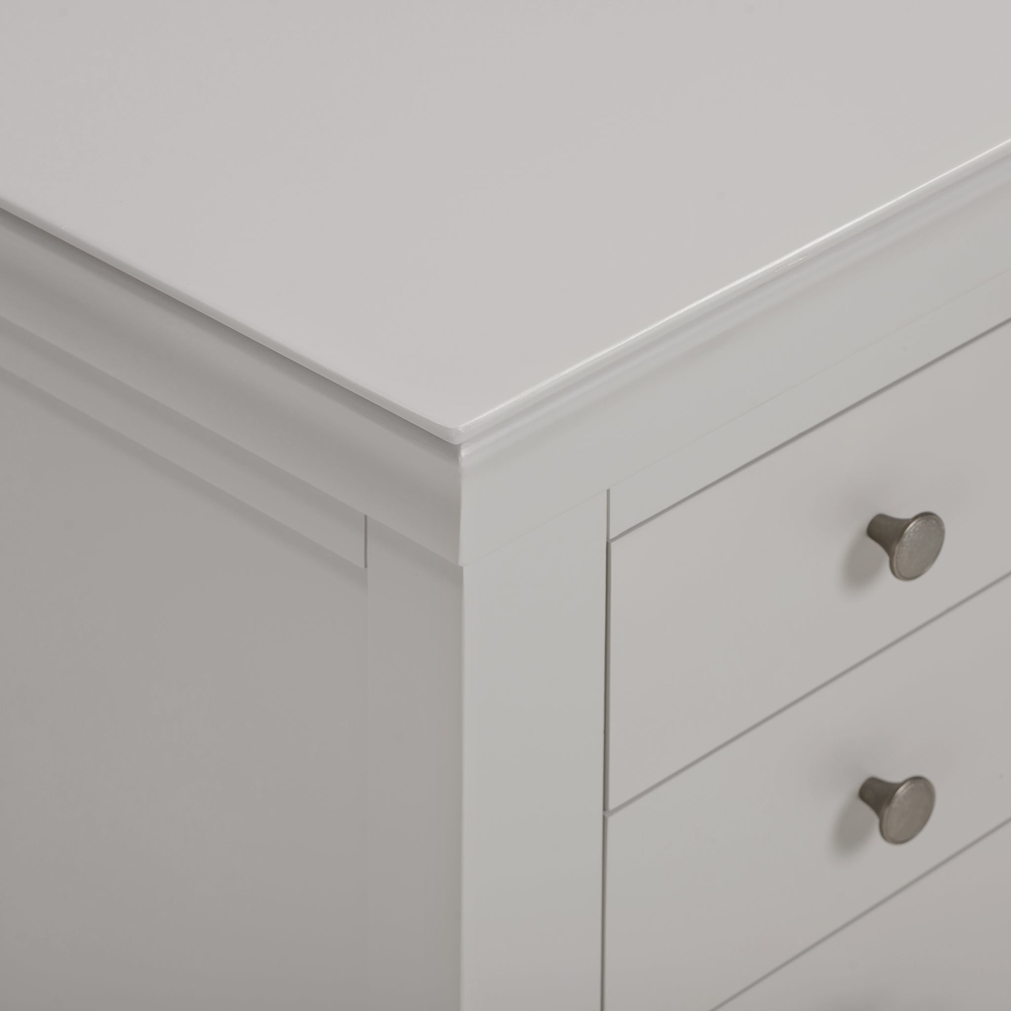 Close-up of a corner of the Chalbury 3 Drawer Bedside Table in Pebble Grey, highlighting its three drawers adorned with silver knobs and a smooth surface.