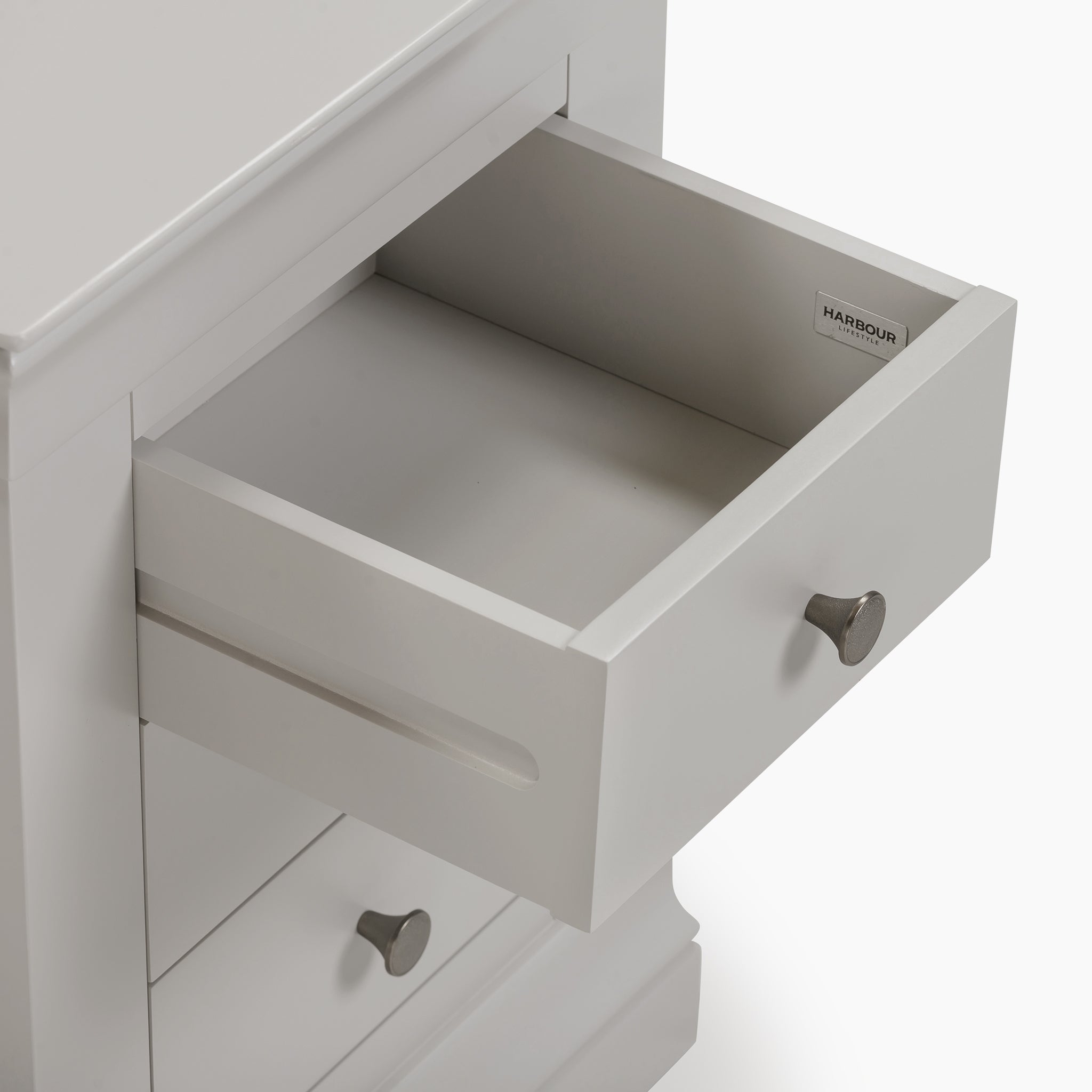 The Chalbury 3 Drawer Bedside Table in Pebble Grey showcases sleek metal handles, with one drawer elegantly open, providing both style and functionality for your bedroom decor.