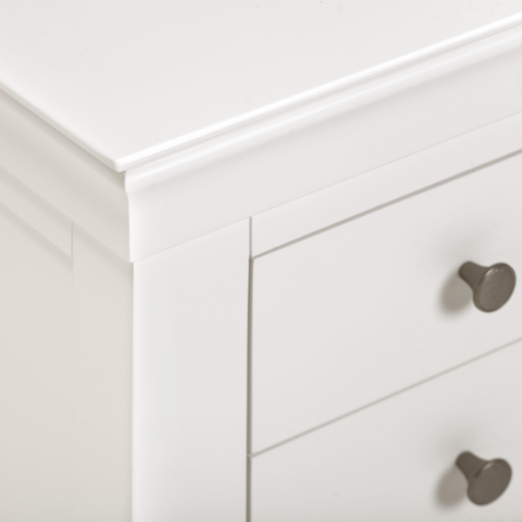 Close-up of the top corner of a Chalbury 3 Drawer Bedside Table in Warm White, highlighting the metal knobs on two visible drawers, which add a touch of elegance to your bedroom décor.