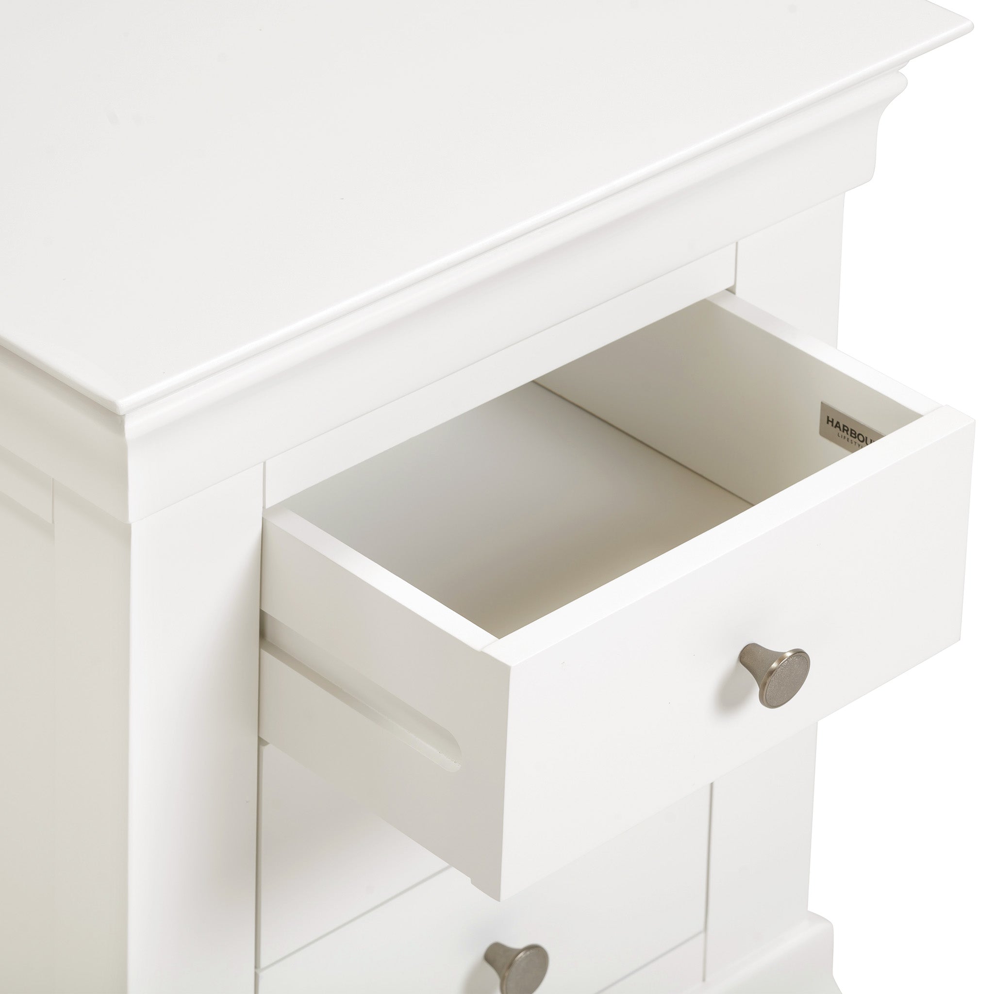 The Chalbury 3 Drawer Bedside Table in Warm White, ideal for enhancing bedroom décor, boasts a classic white wooden finish with three open drawers and elegant silver knobs.