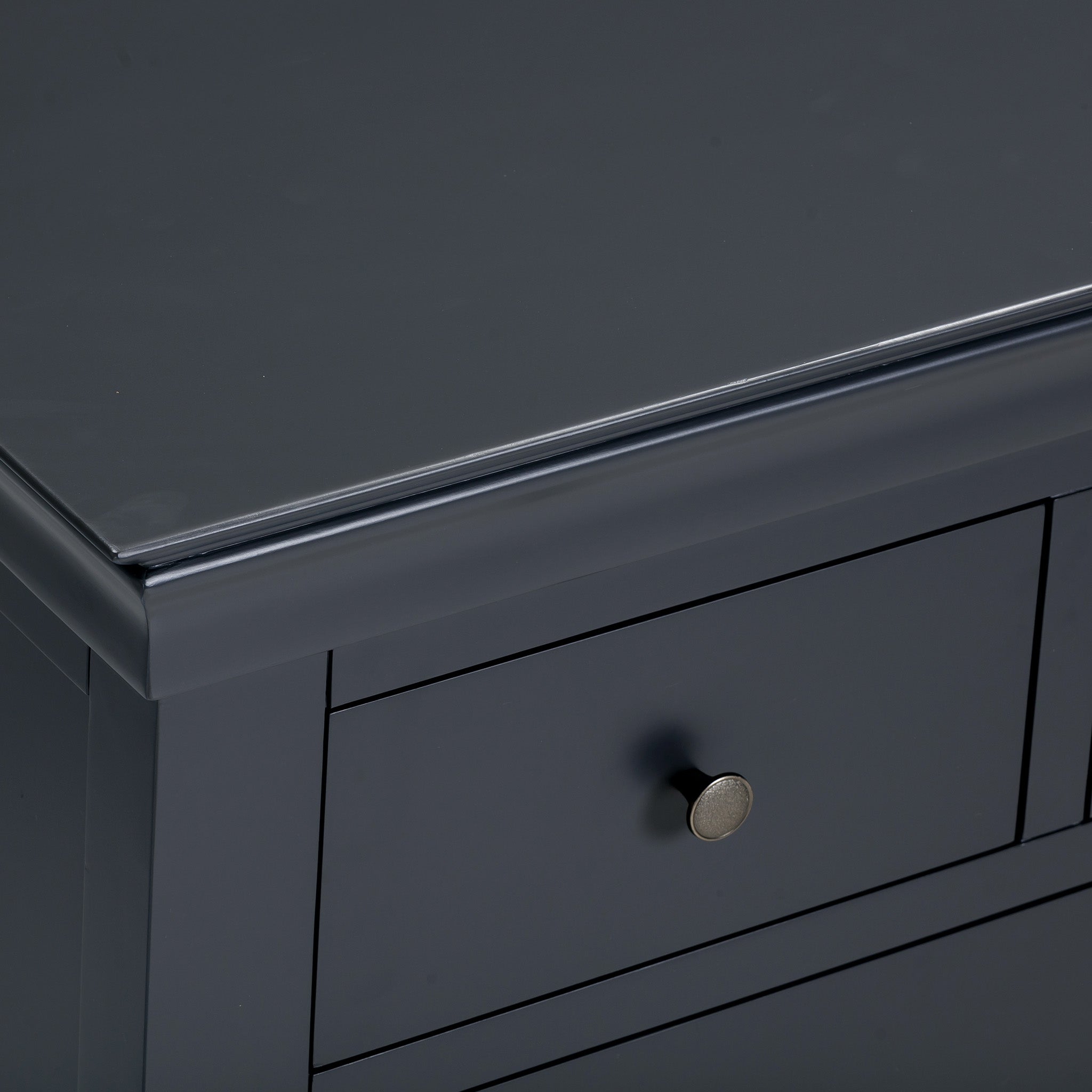 Close-up of a corner of the Chalbury 2 Over 3 Chest of Drawers in Dusky Black, showcasing a drawer with a round metallic knob that reflects modern design.