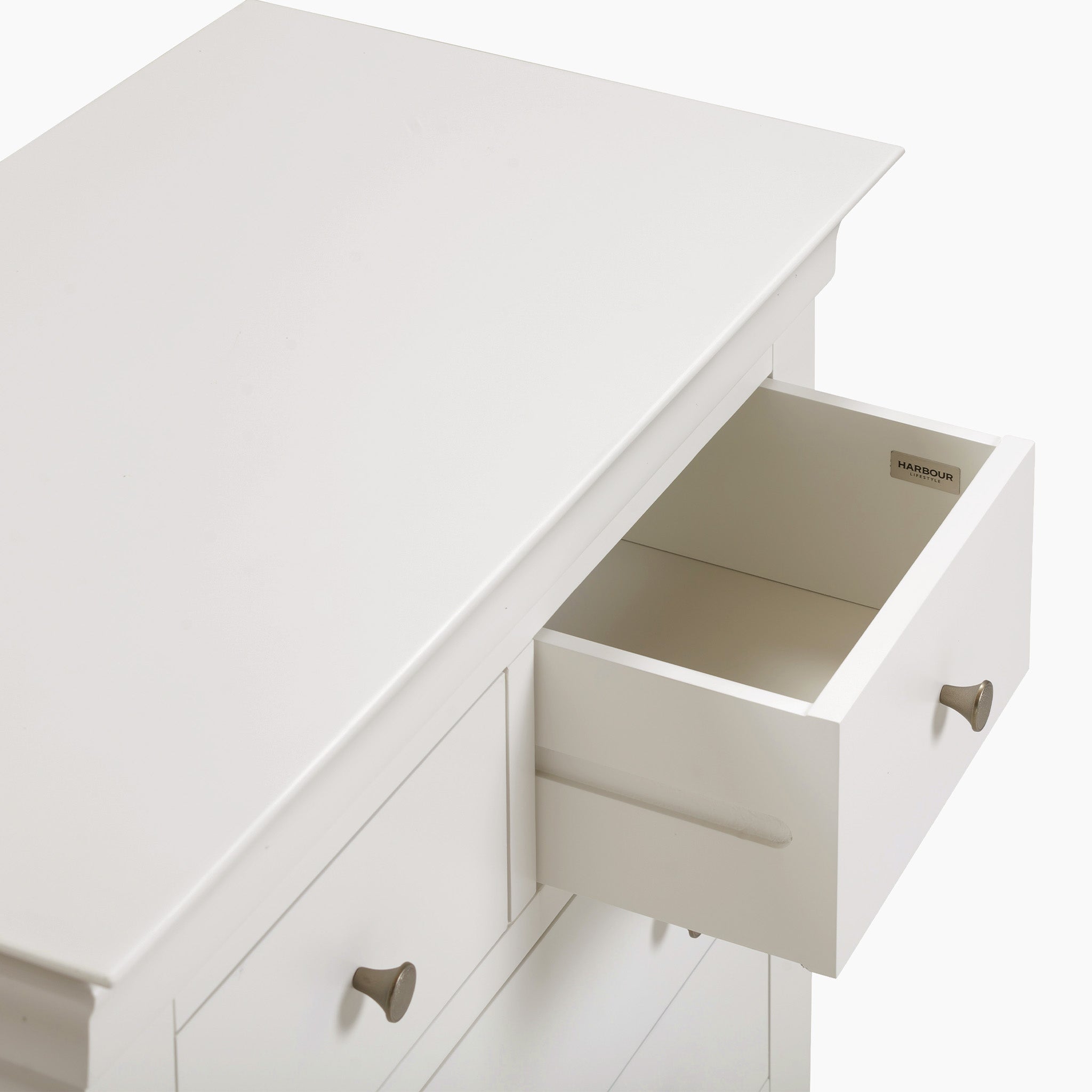 Chalbury 2 Over 3 Chest of Drawers in Warm White features an open drawer with elegant silver knobs on both the drawer and cabinet doors. This modern design provides ample storage to maintain a tidy and stylish space.