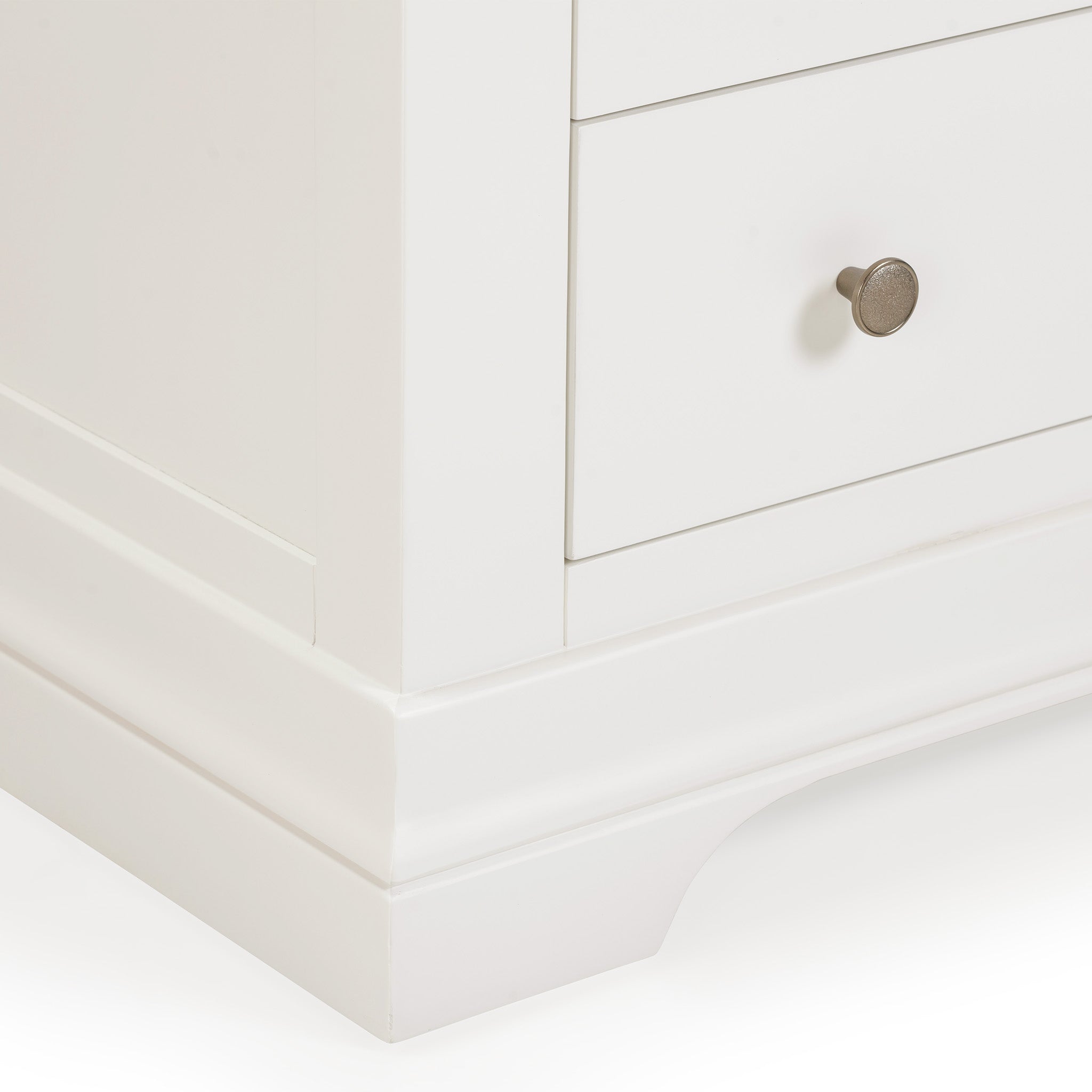 A detailed view of the Chalbury 3 Over 4 Chest of Drawers in warm white showcases a stylish corner with dual drawers and a circular silver knob on one. This sophisticated piece enhances your storage furniture collection with its polished design.