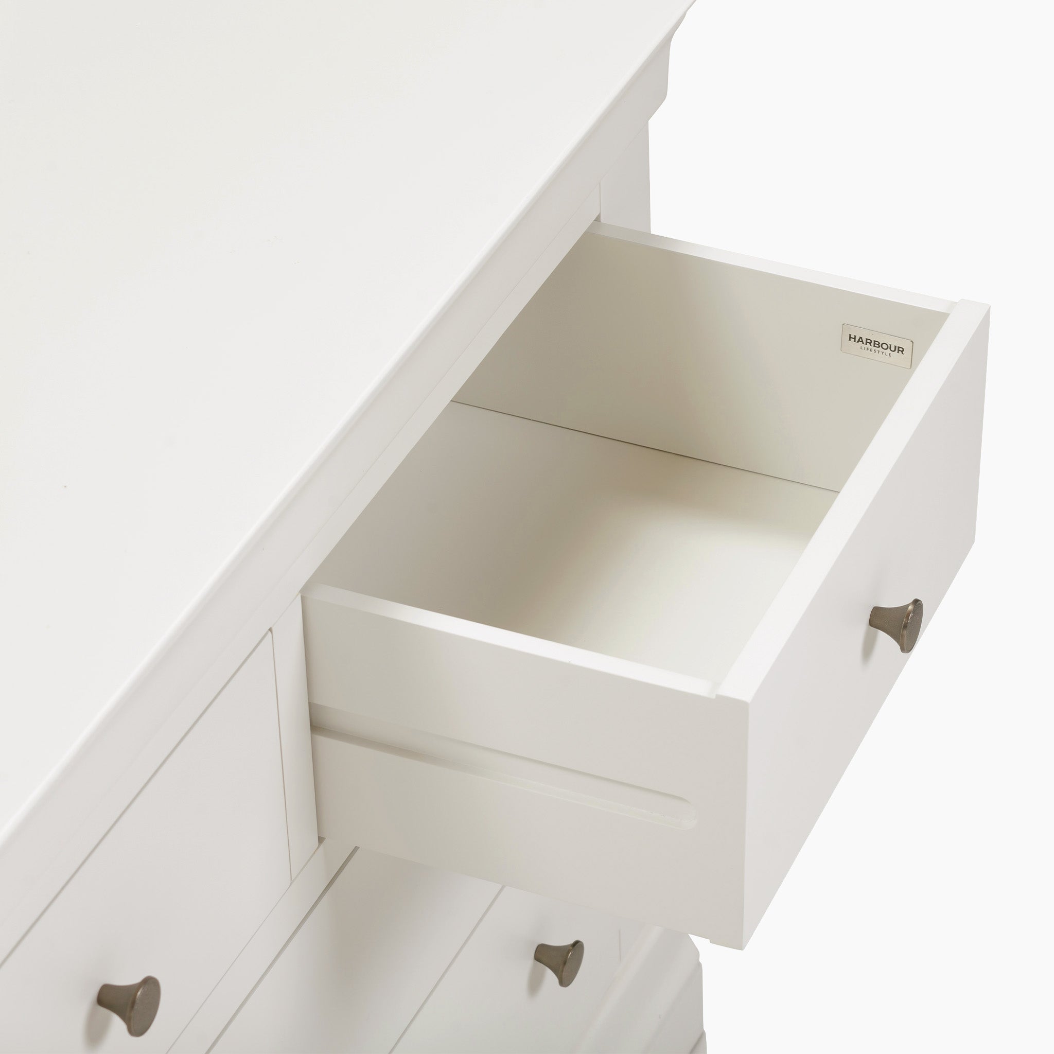 The Chalbury 3 Over 4 Chest of Drawers in Warm White features an open drawer with sleek silver handles, seamlessly blending style and functionality as a piece of storage furniture.