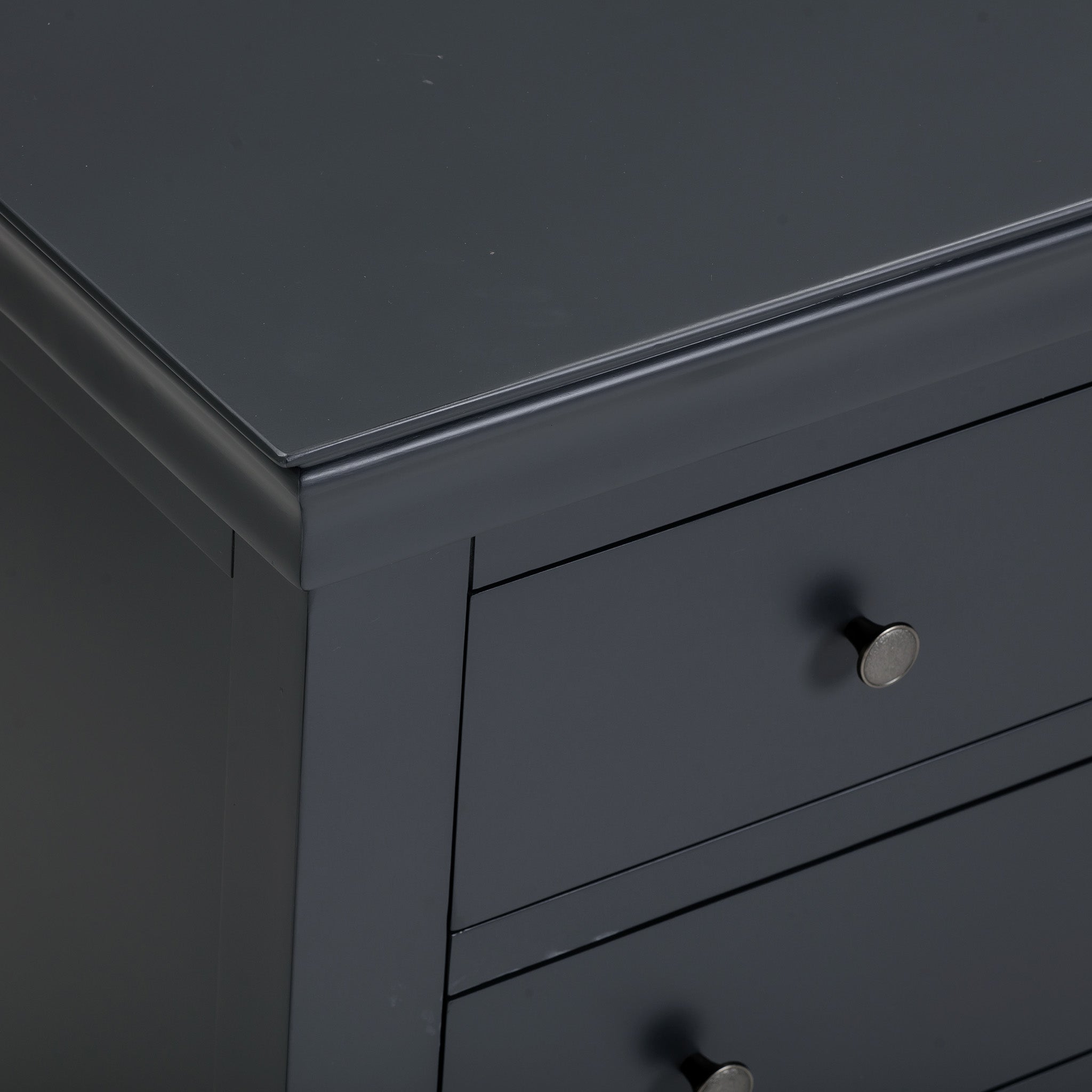 The dark gray Chalbury 3 Over 4 Chest of Drawers in Dusky Black corner reveals two drawers adorned with round dusky black knobs, showcasing a perfect blend of elegance and simplicity.