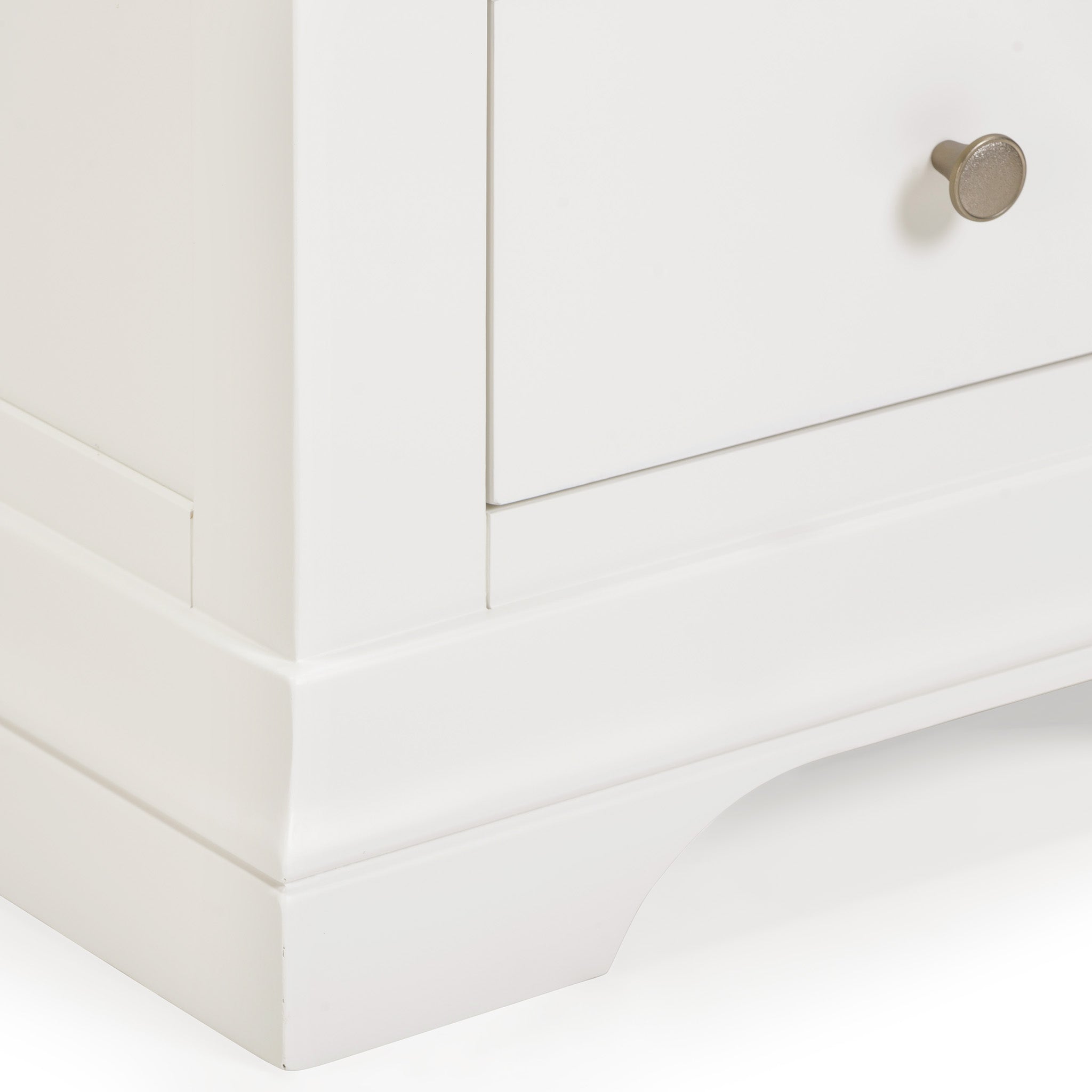 The Chalbury 5 Chest of Drawers in Warm White stands elegantly in the corner, showcasing its stylish finish. This piece of storage furniture includes a round metal knob on each drawer, combining functionality with timeless design.