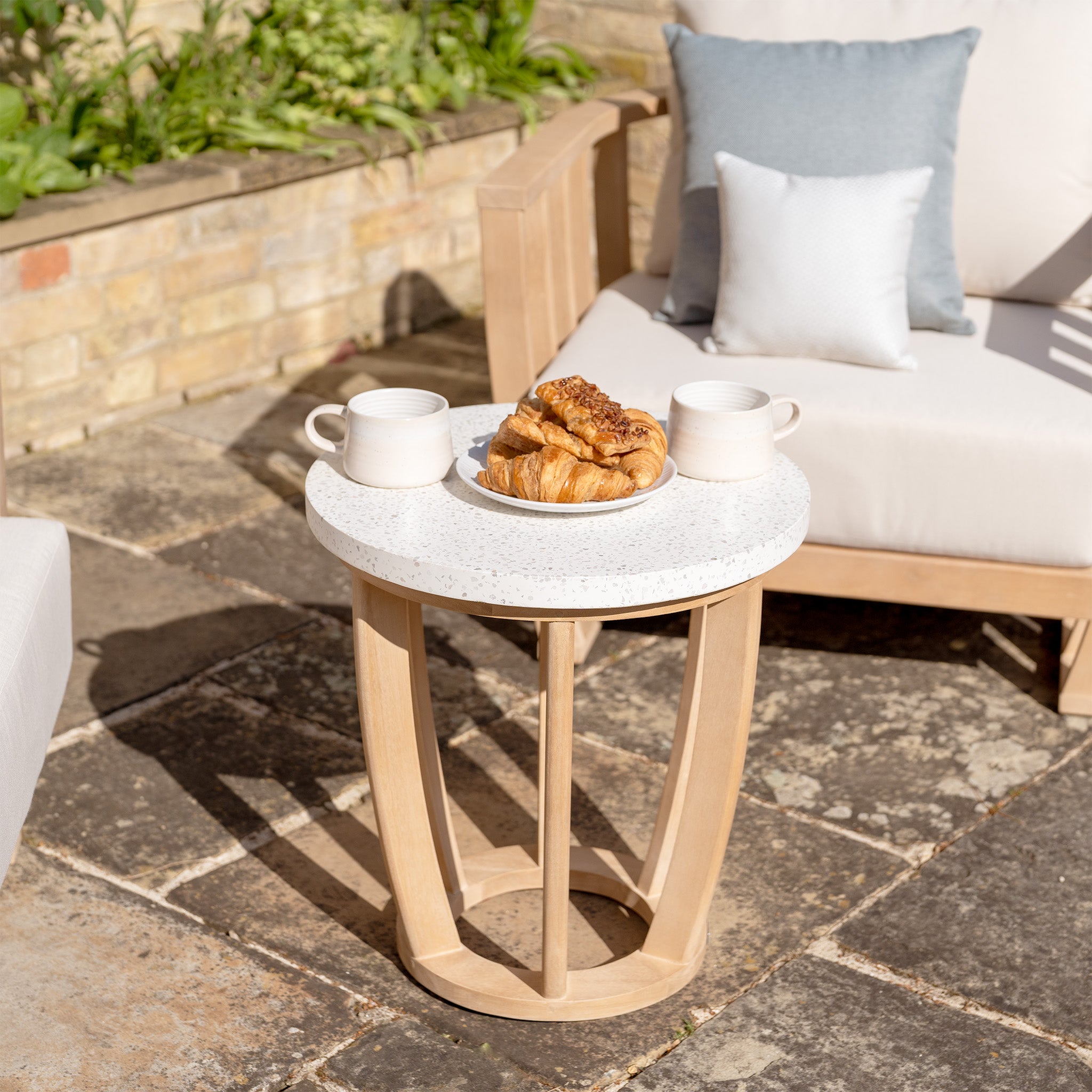 A small outdoor table with two coffee cups and a plate of croissants, surrounded by the Cape Lounge Set in Beige with deep plush cushions, all basking in the sun.