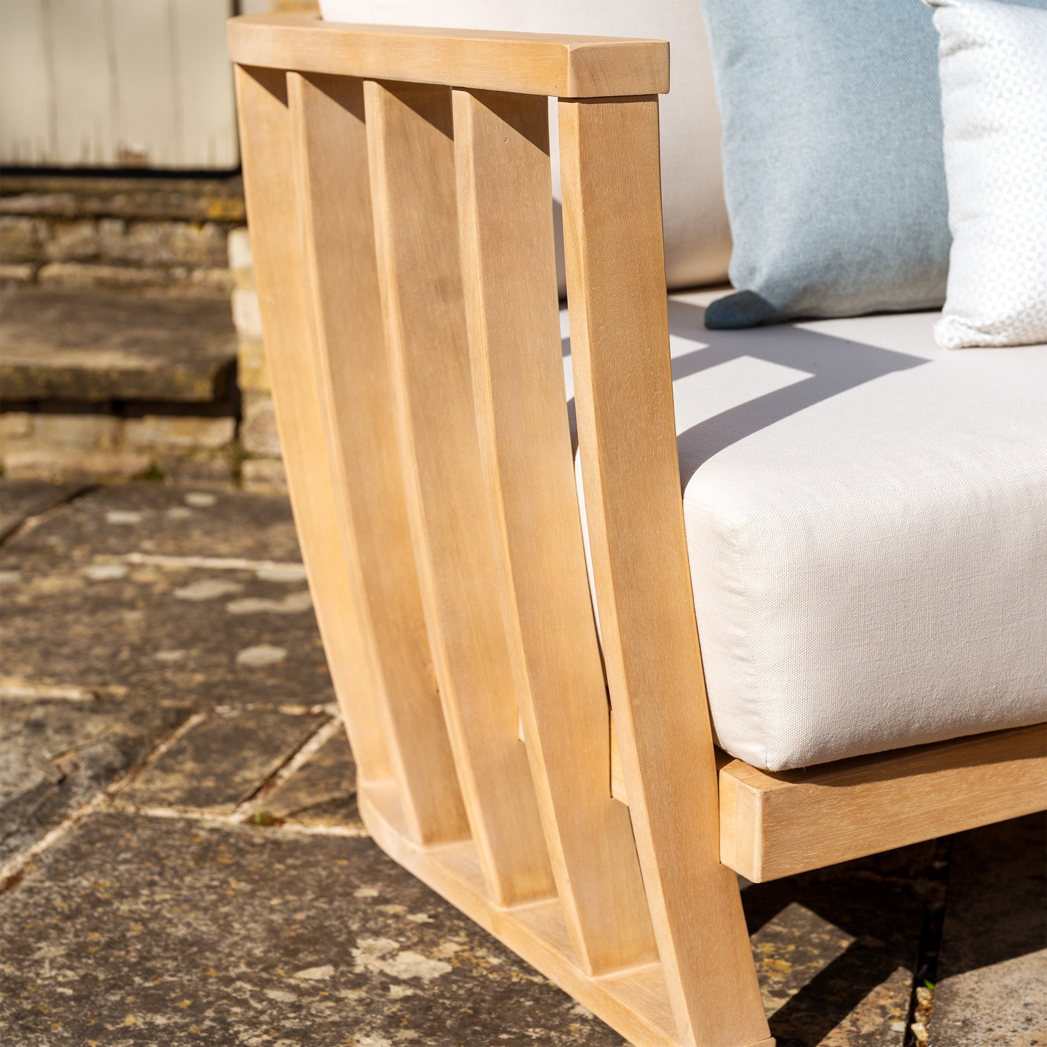 Close-up of the arm of a Cape Lounge Set in Beige, featuring deep plush white cushions and a light blue pillow, set on a stone patio.