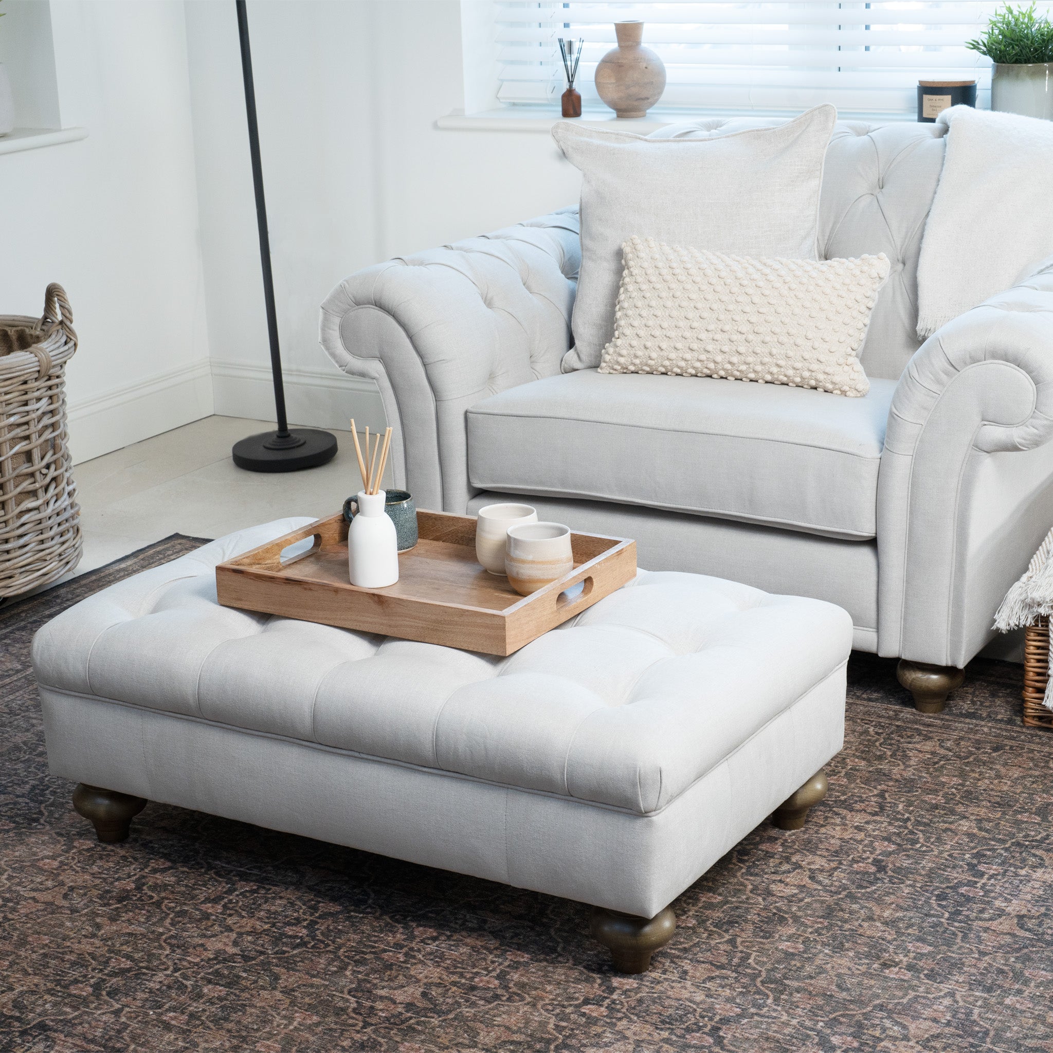 Cozy living room with a white armchair, a Warm Grey Chesterfield Footstool, wooden tray, and decor on a patterned rug.