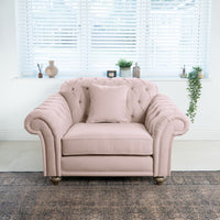 Chesterfield Loveseat in Dusky Pink with a cushion, positioned on a patterned rug, in front of a window adorned with blinds and decor items.