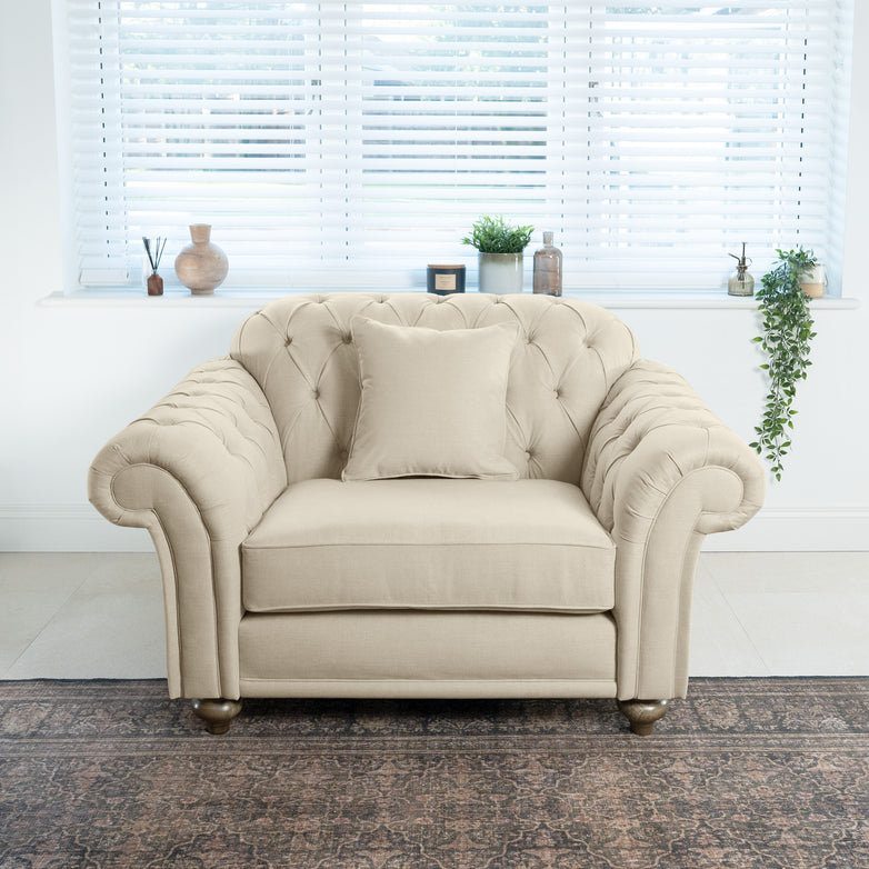 A Chesterfield Loveseat in beige sits elegantly in front of a window, adorned with decorative items and plants on the sill.