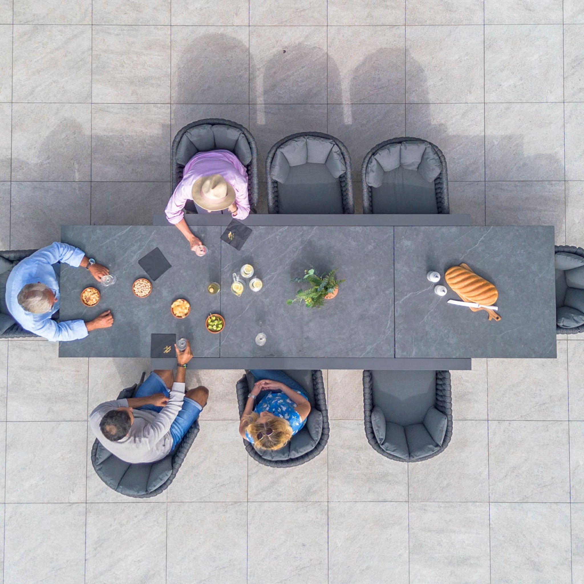 Top view of four people sitting around a Palma 8 Seat Rope Extending Dining Set in Grey with snacks, a plant, and a loaf of bread placed on it.