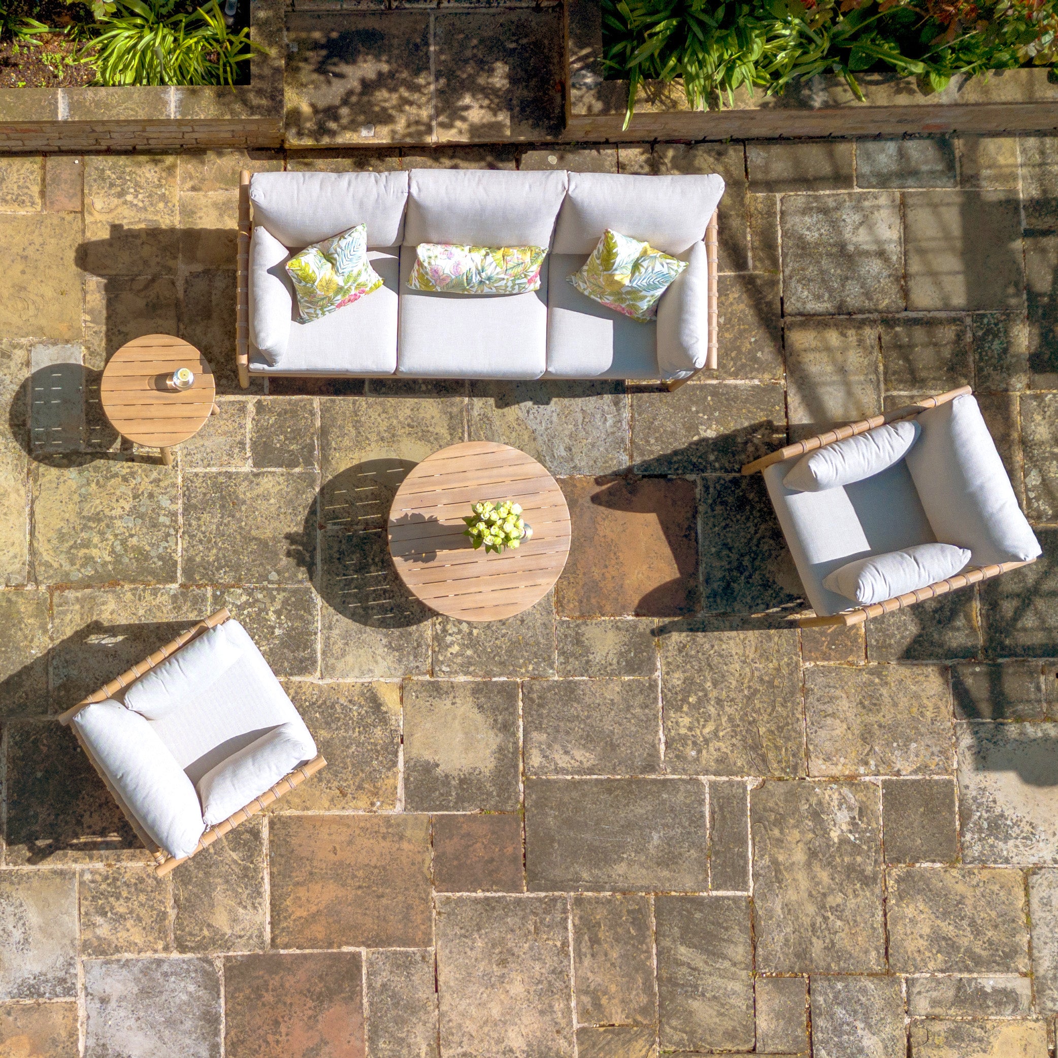 Overhead view of the Paia 3 Seat Sofa Set in Linen, which includes a sofa, two chairs, tables, and cushions made from water-resistant polyester on a stone floor.