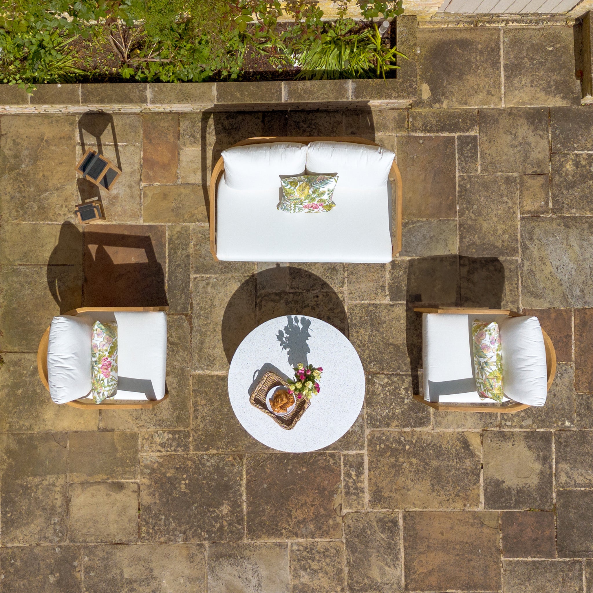 Aerial view of outdoor patio with the Yosemite 2 Seat Sofa Set In Glacier, featuring four white cushioned seats around a round table set on stone tiles, with premium teak wood accents.