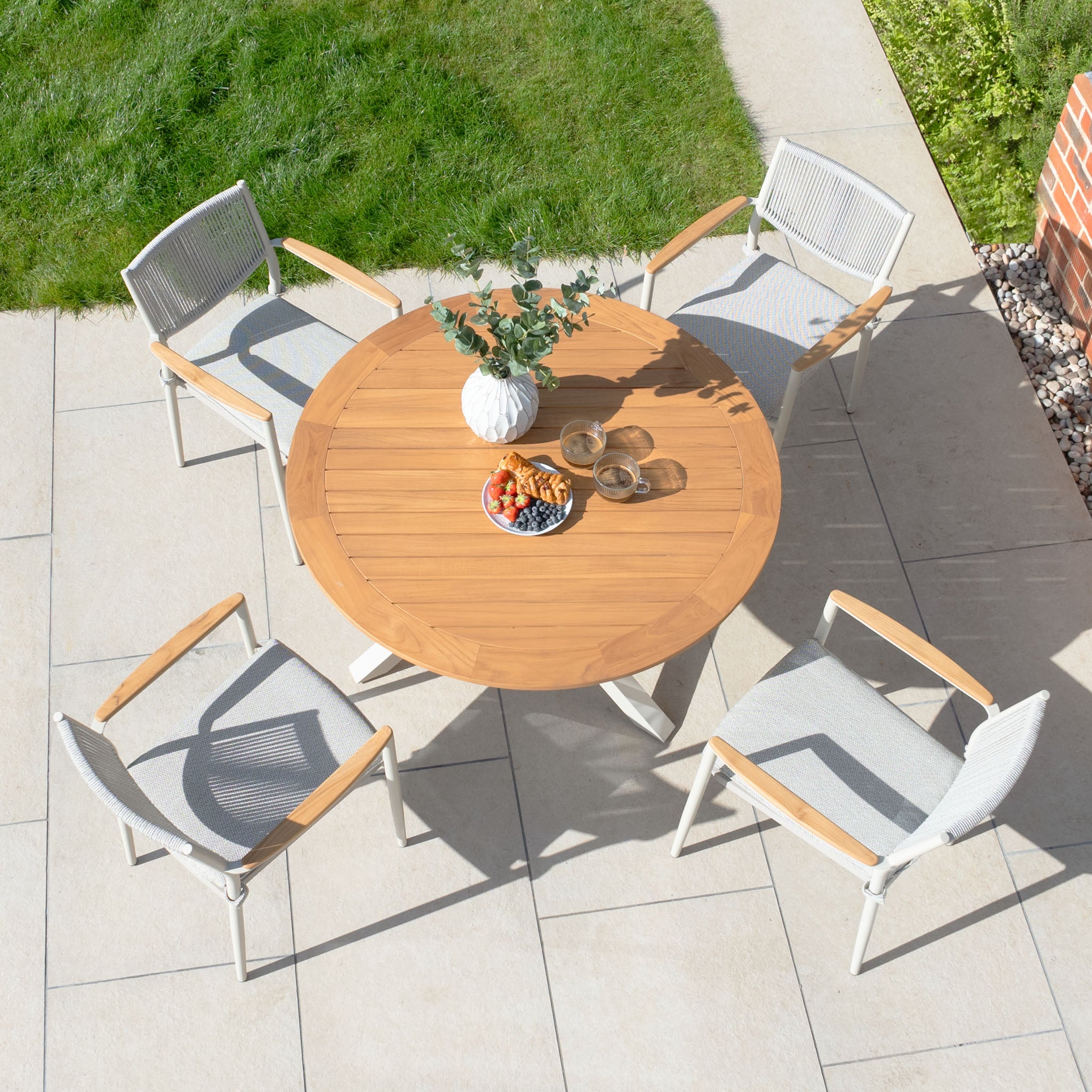 Top view of the Tellaro 4 Seat Round Dining Set in Latte, featuring a teak table and four chairs crafted with weather-resistant rope, with a vase containing greenery placed in the center.